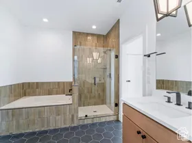 Bathroom featuring a built-in tub, glass-enclosed shower, wood-look tiled walls, and a single vanity with a white countertop