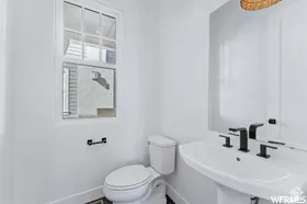 White powder room featuring a pedestal sink with matte black fixtures, a wall-mounted rectangular mirror, and a single-pane window with white trim