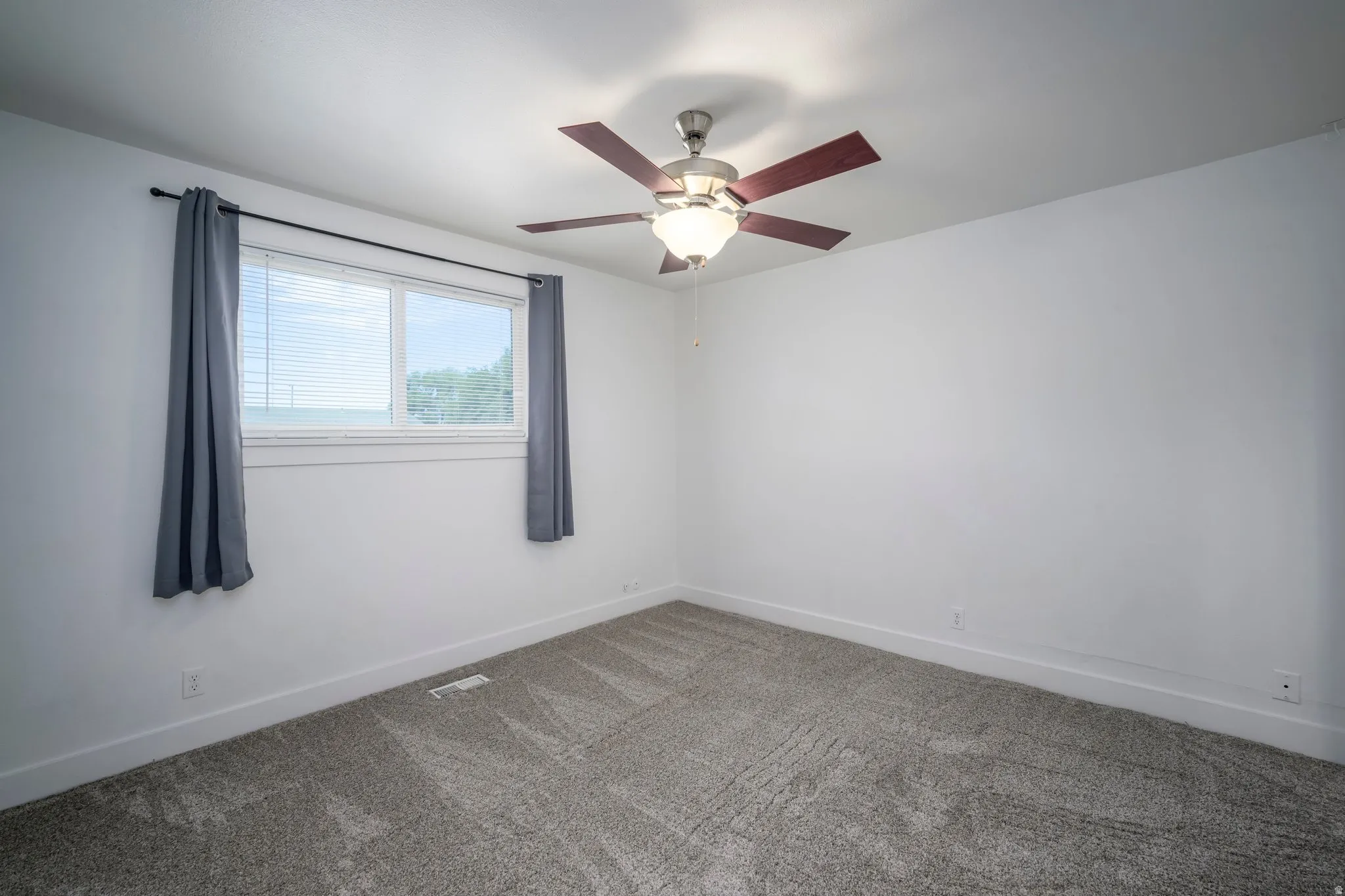 Spacious room featuring neutral carpeting, a ceiling fan with integrated lighting, and a double window providing natural illumination