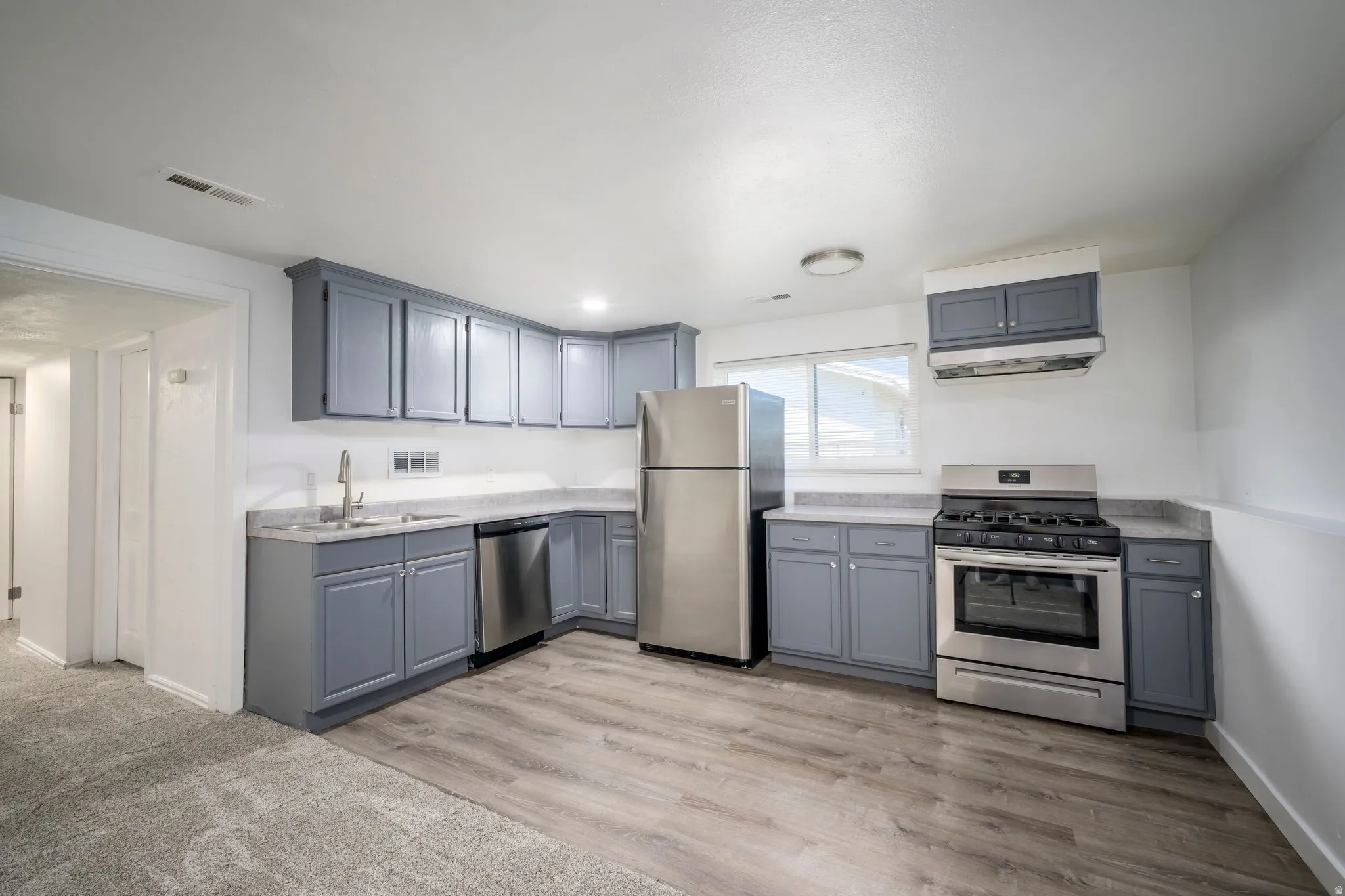 Kitchen featuring gray cabinetry, light countertops, wood-finish flooring, and stainless steel appliances including a refrigerator, dishwasher, and range
