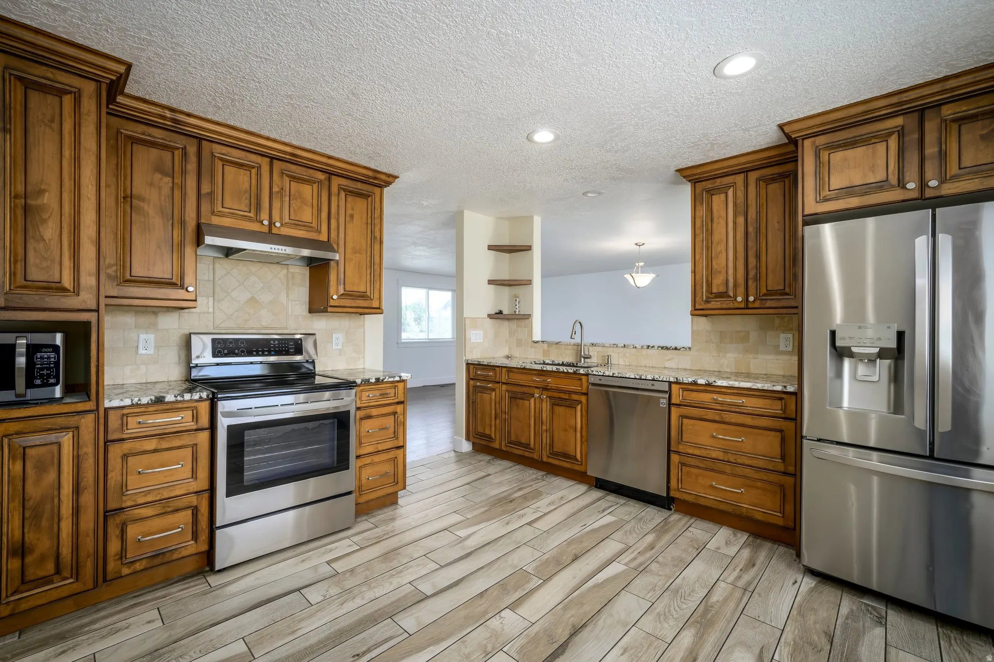 Kitchen featuring wood-finish cabinetry, stainless steel appliances, granite-style countertops, tile backsplash, and wood-look plank flooring