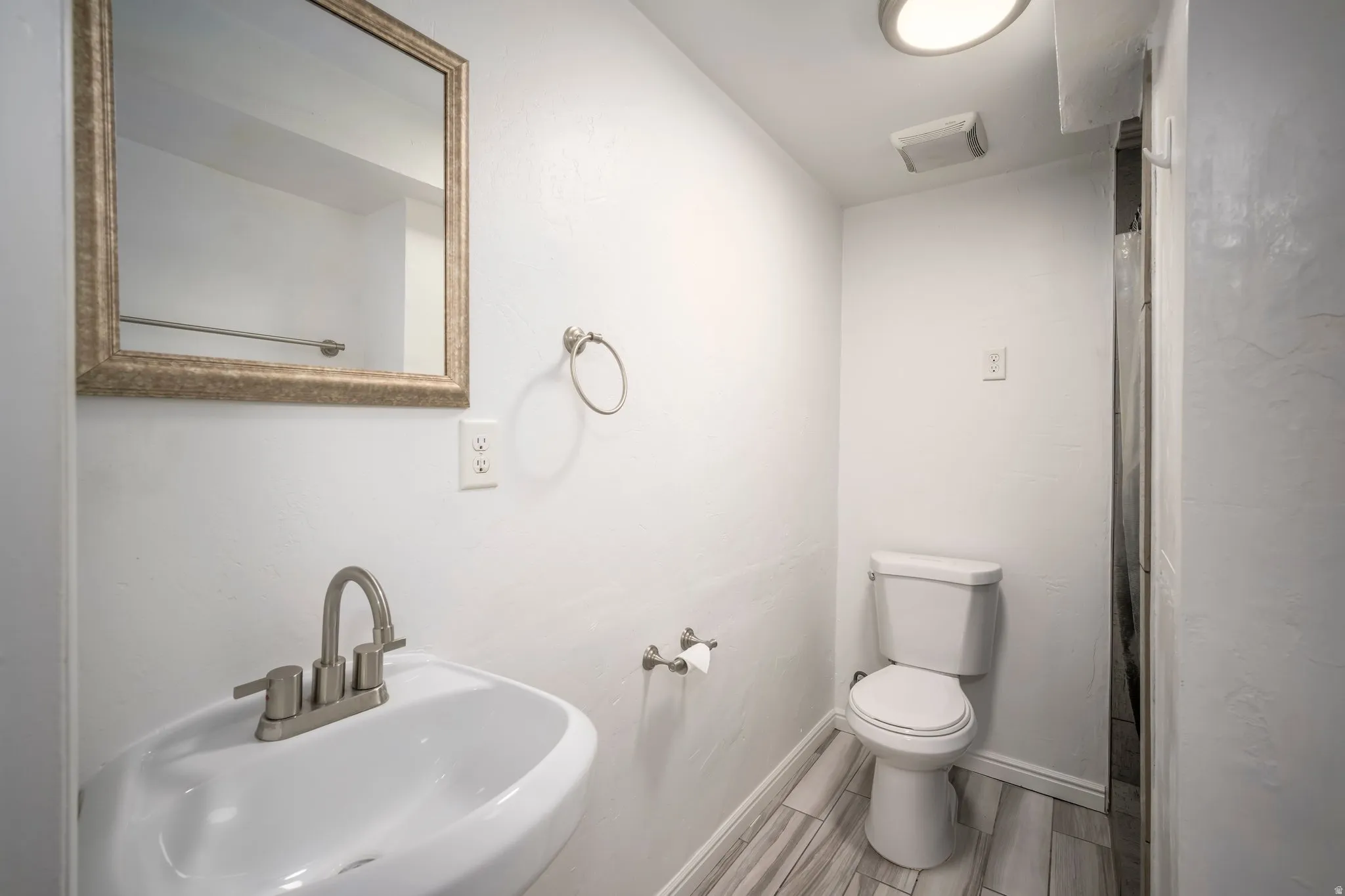 Bathroom featuring a pedestal sink, brushed nickel faucet, framed mirror, and wood-finish flooring