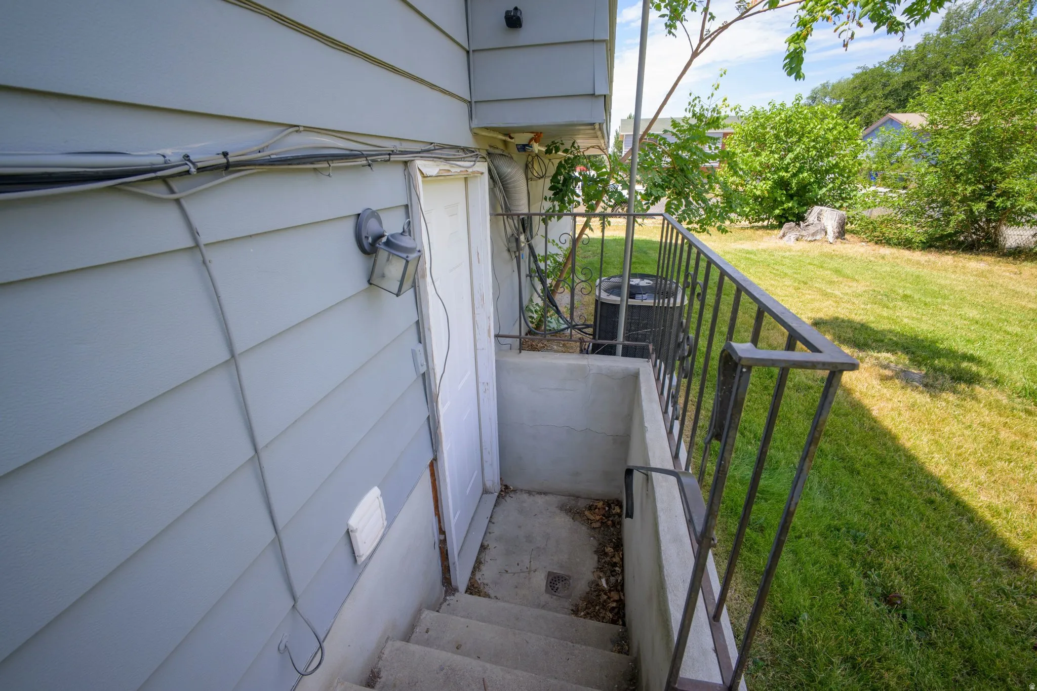 Concrete basement entry with a metal handrail, exterior siding, and a security light