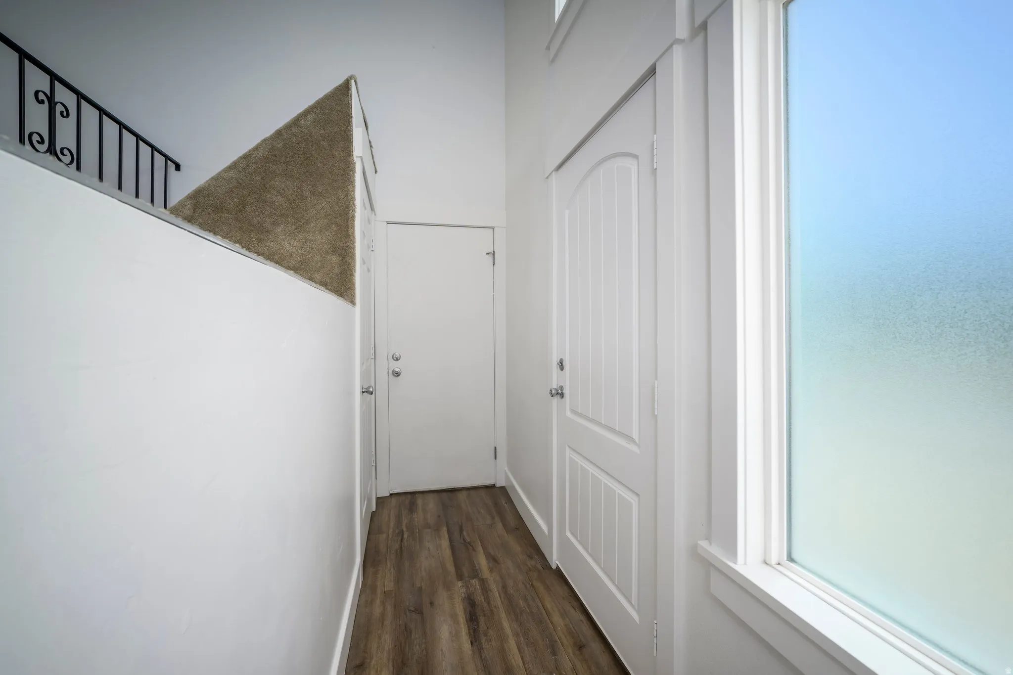Spacious interior hallway featuring wood-finish flooring, white walls, and a large frosted window