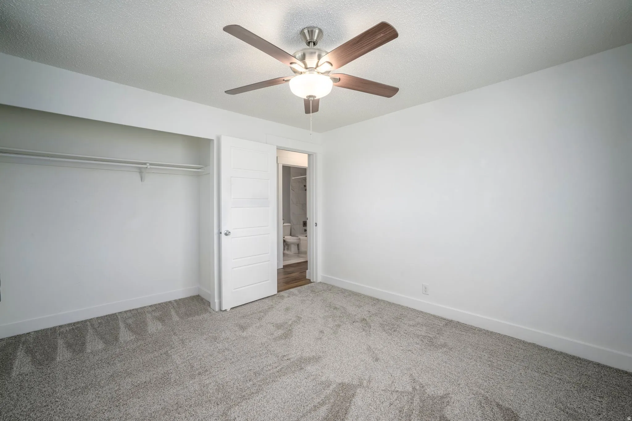 Bedroom with textured gray carpet, white walls, and a ceiling fan with wood-finish blades