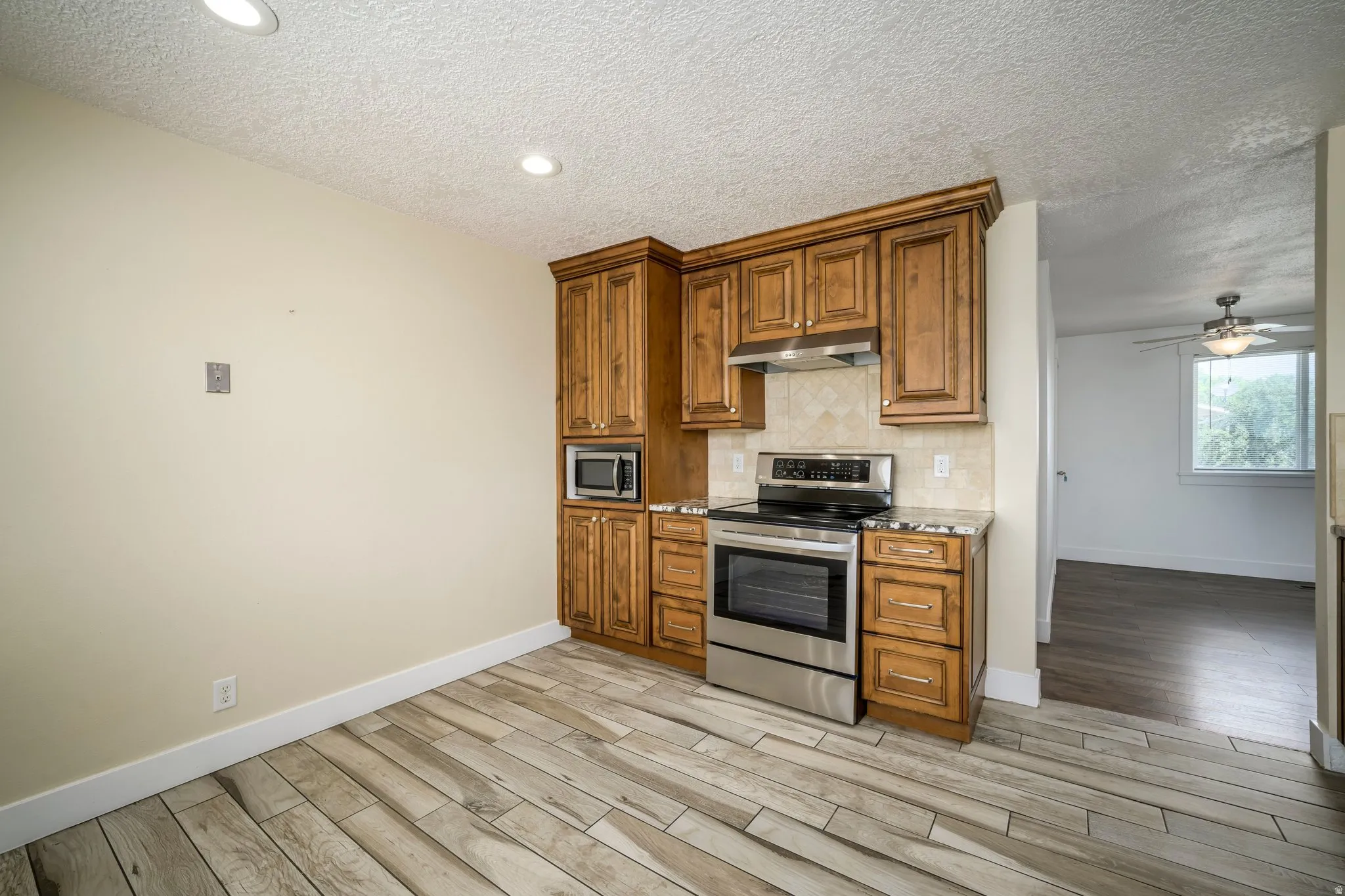 Kitchen area featuring wood-finish flooring, recessed lighting, wood cabinetry, stainless steel appliances, and a tiled backsplash