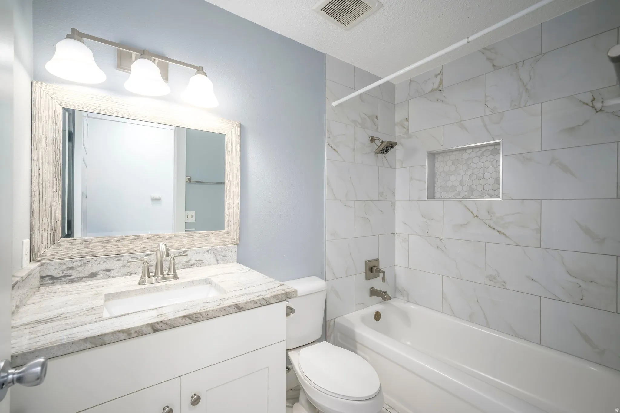 Bathroom featuring a white vanity with a stone-finish countertop, integrated rectangular sink, brushed nickel faucet, and a large framed mirror with overhead vanity lighting