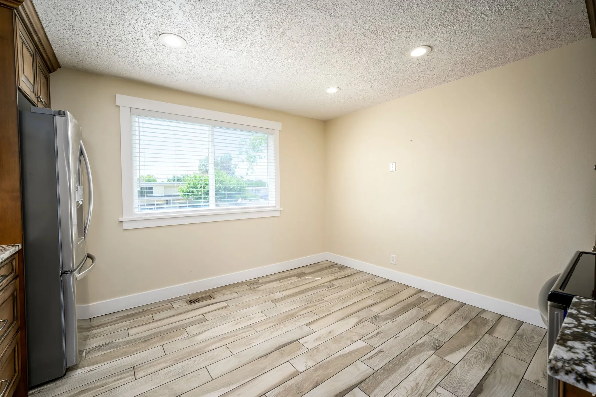Open room featuring wood-finish tile flooring, recessed ceiling lighting, a window with blinds, and neutral wall paint