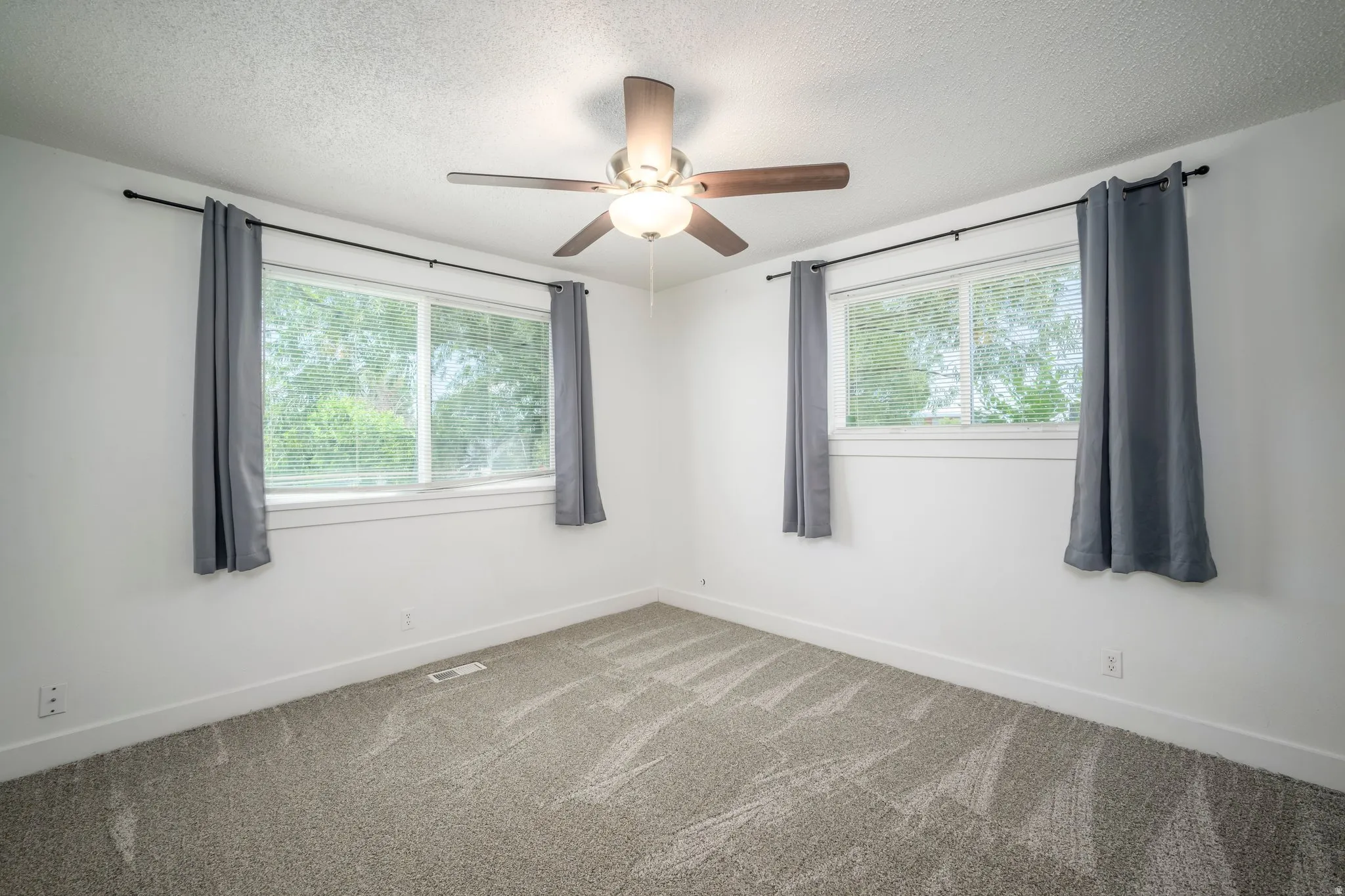 Bright room featuring two windows with white blinds, neutral carpeting, white walls, and a ceiling fan with integrated lighting