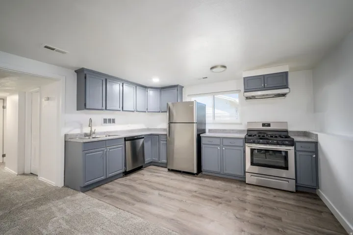 Kitchen featuring gray cabinetry, light countertops, wood-finish flooring, and stainless steel appliances including a refrigerator, dishwasher, and range