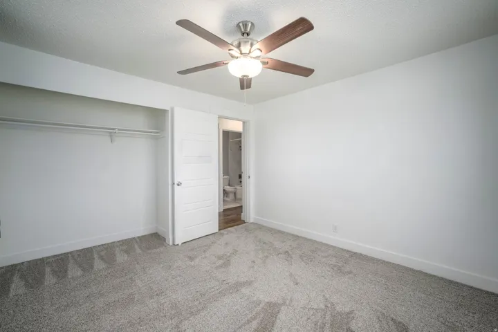 Bedroom with textured gray carpet, white walls, and a ceiling fan with wood-finish blades