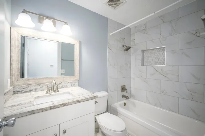 Bathroom featuring a white vanity with a stone-finish countertop, integrated rectangular sink, brushed nickel faucet, and a large framed mirror with overhead vanity lighting