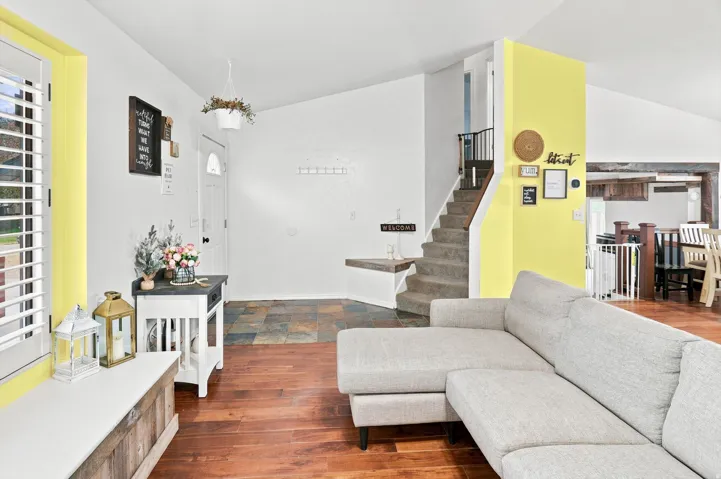 Living area featuring wood-finish flooring, vaulted ceilings, and a staircase with carpeted treads