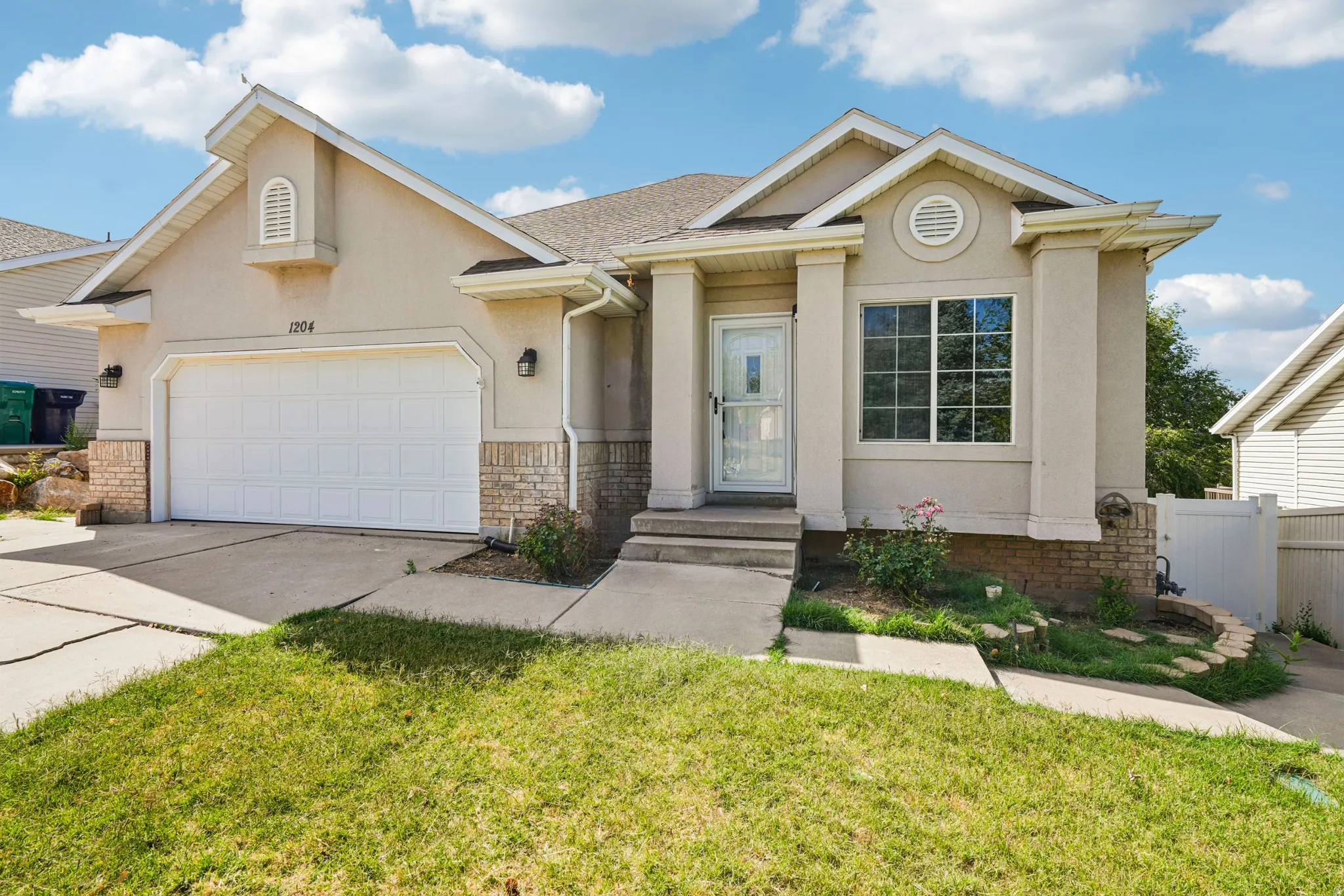 Stucco exterior home featuring a two-car garage, brick accents, and a covered entry