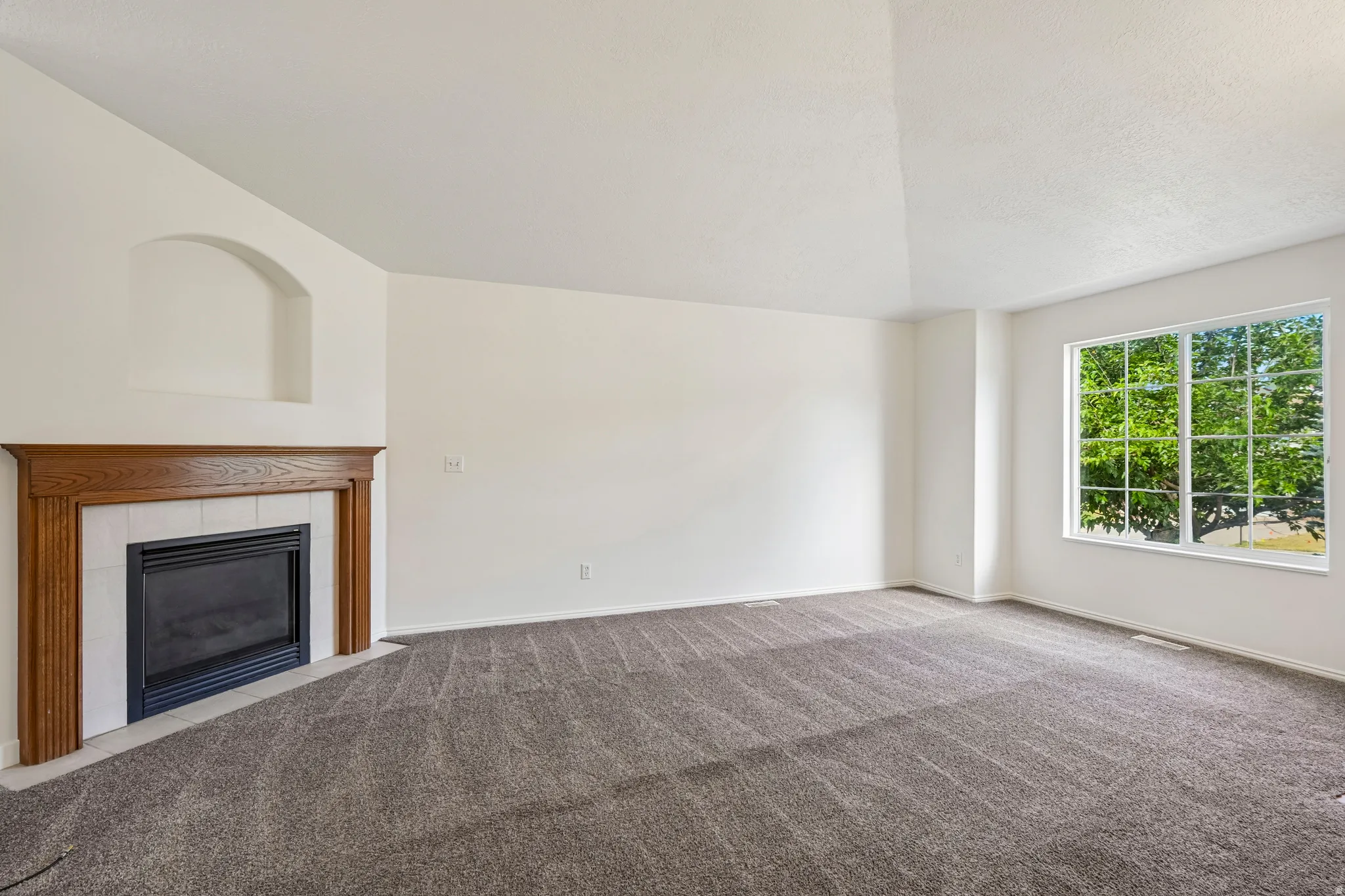 Living area featuring a fireplace with a wood-finish mantel and tile surround, an arched wall niche, vaulted ceiling, and a large multi-pane window
