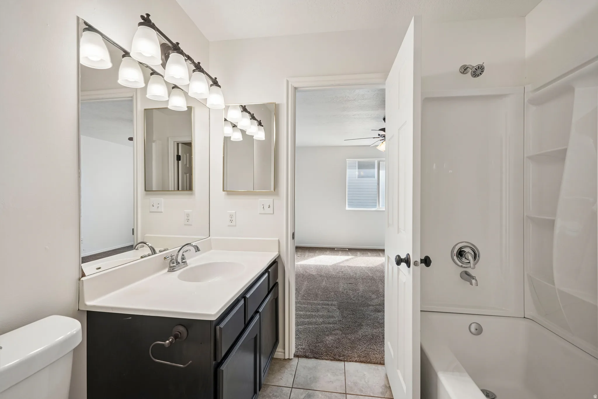White vanity featuring a white countertop, dual basin sink, and an integrated shower-tub combination with white tile-finish flooring