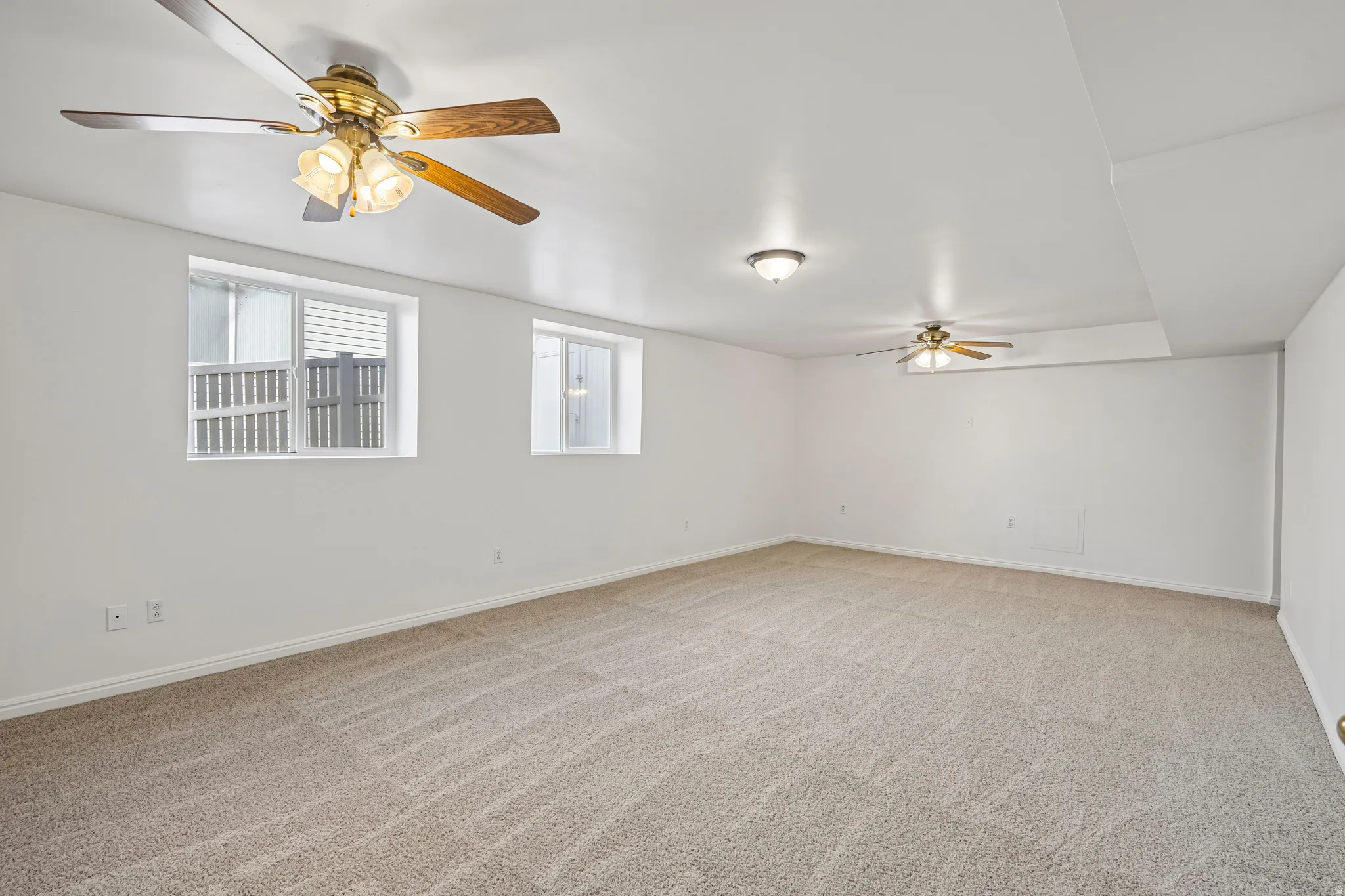 Spacious room featuring neutral carpeting, white walls, and two ceiling fans with integrated lighting
