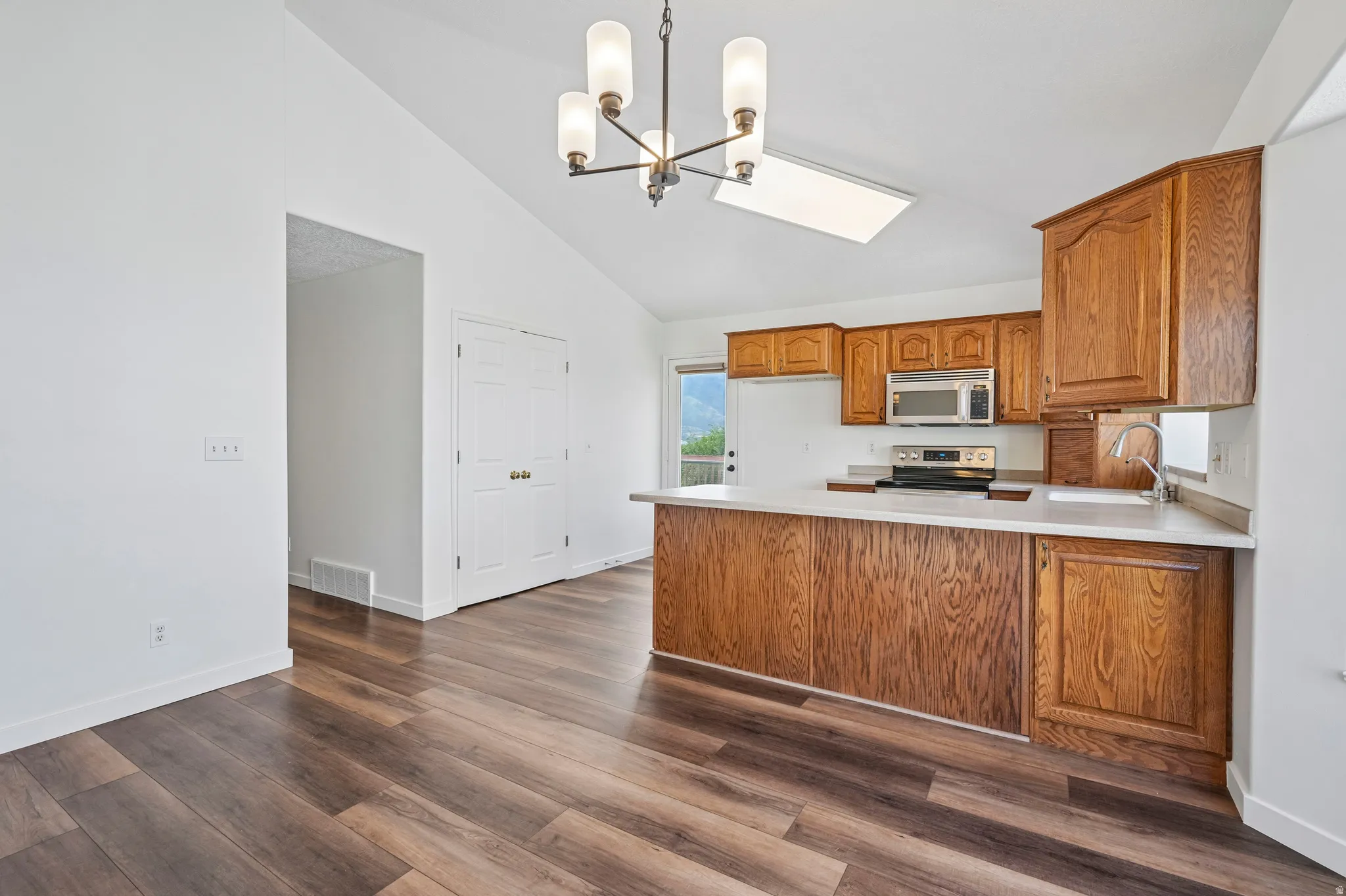 Open-concept kitchen and dining area featuring wood-finish flooring, vaulted ceilings, and a contemporary chandelier