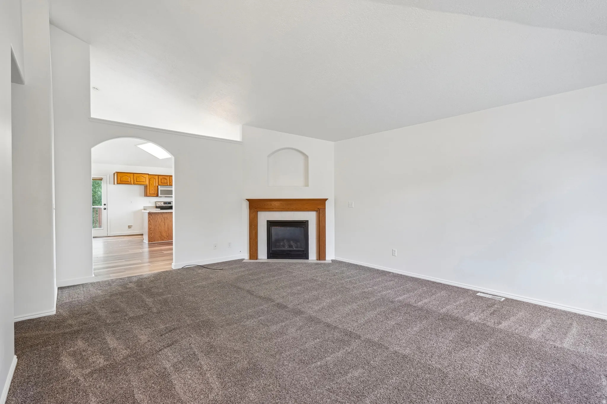 Spacious living area featuring neutral carpeting, a fireplace with wood mantel, and an arched entryway