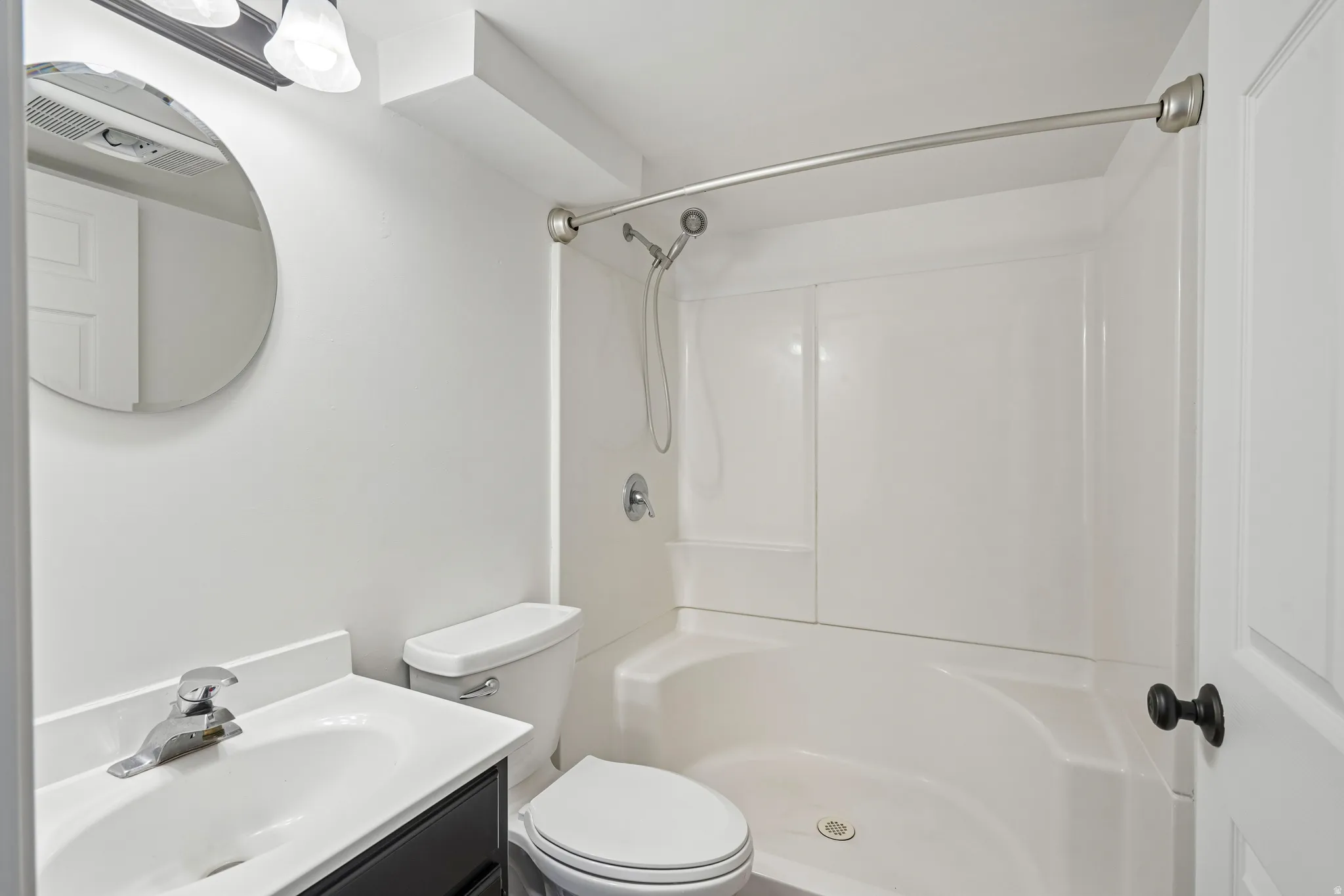 Bathroom featuring a white integrated tub and shower unit, a dark wood-finish vanity with an integrated sink and white countertop, a circular mirror, and a modern two-light vanity fixture