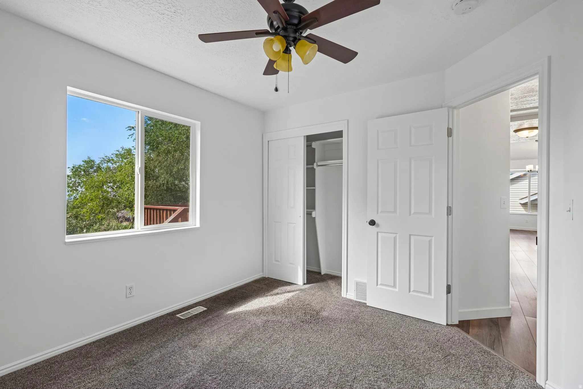 Carpeted room featuring a ceiling fan with integrated lighting, a large window, and a built-in closet with bi-fold doors