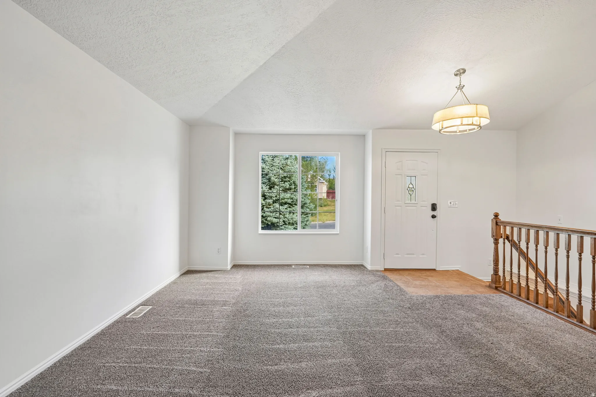 Inviting entry area featuring a white front door with decorative glass, a contemporary drum pendant light, and a wood baluster railing