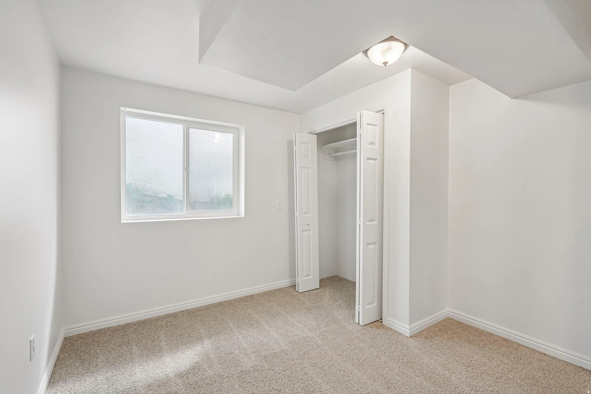 Room featuring a window, neutral-toned carpet, white walls, and a bi-fold door closet