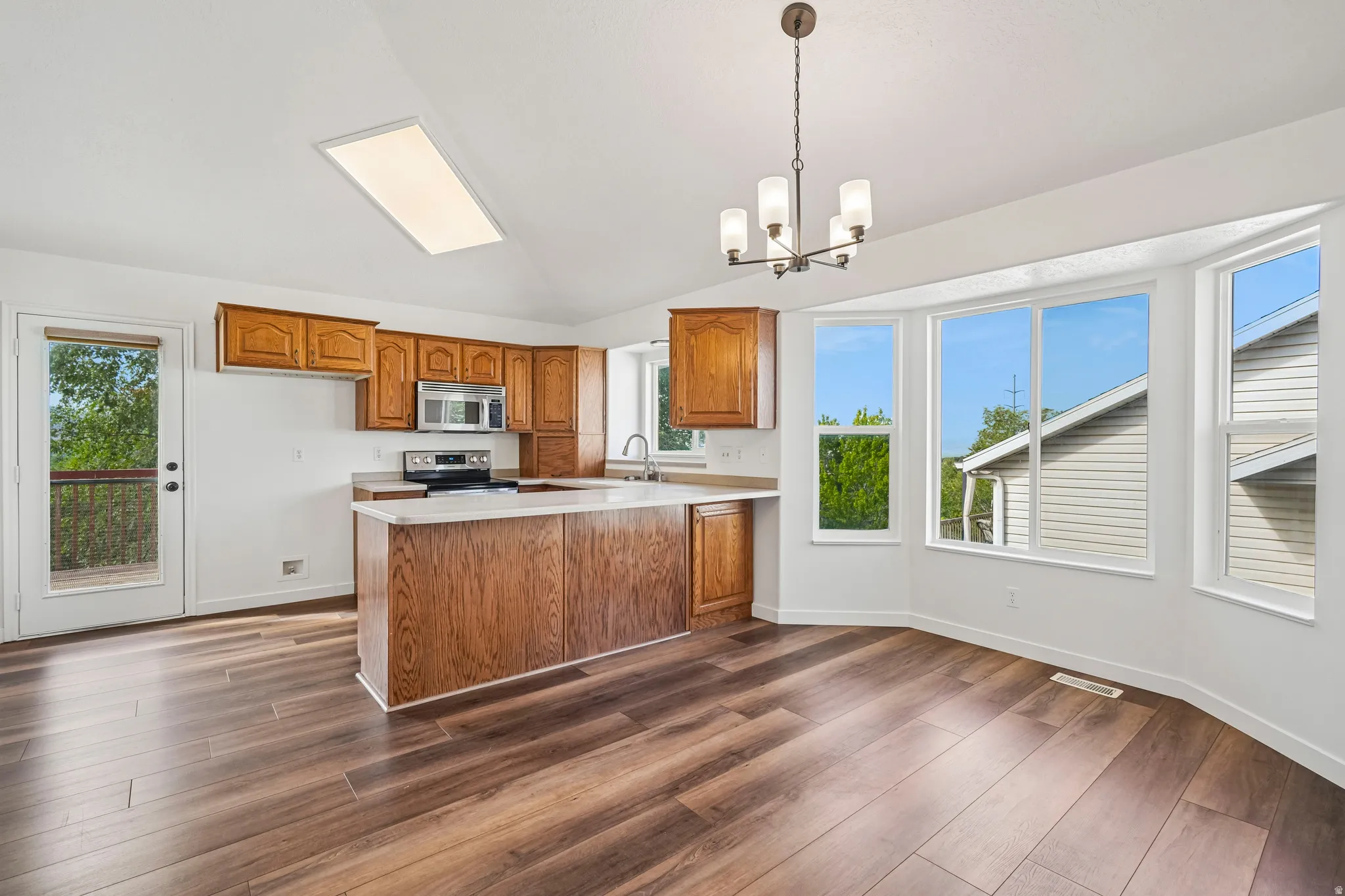 Open-concept kitchen and dining area featuring wood-finish flooring and a vaulted ceiling