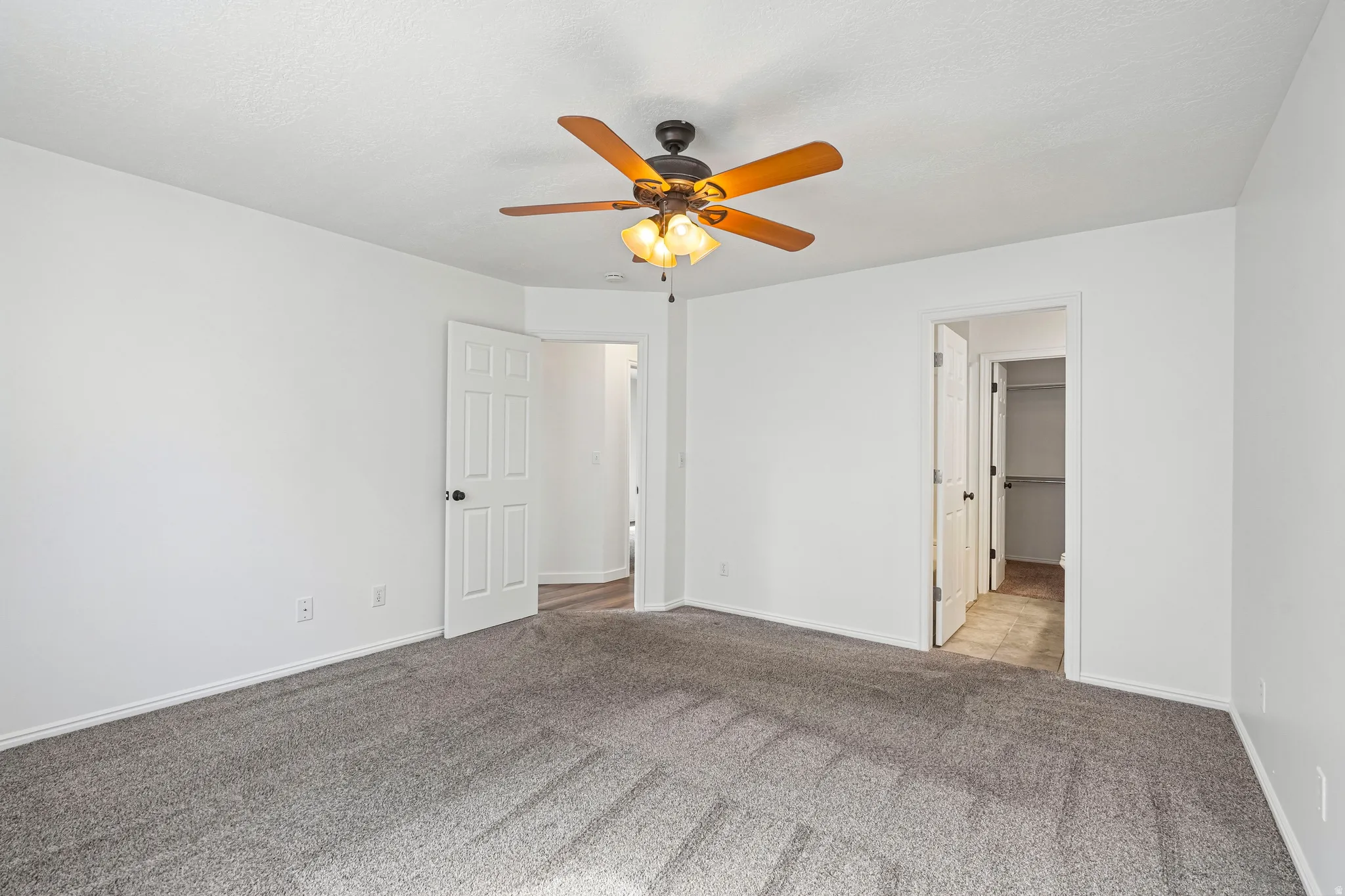 Spacious room featuring neutral carpeting, white walls, a ceiling fan with light fixture, and a built-in closet with shelving