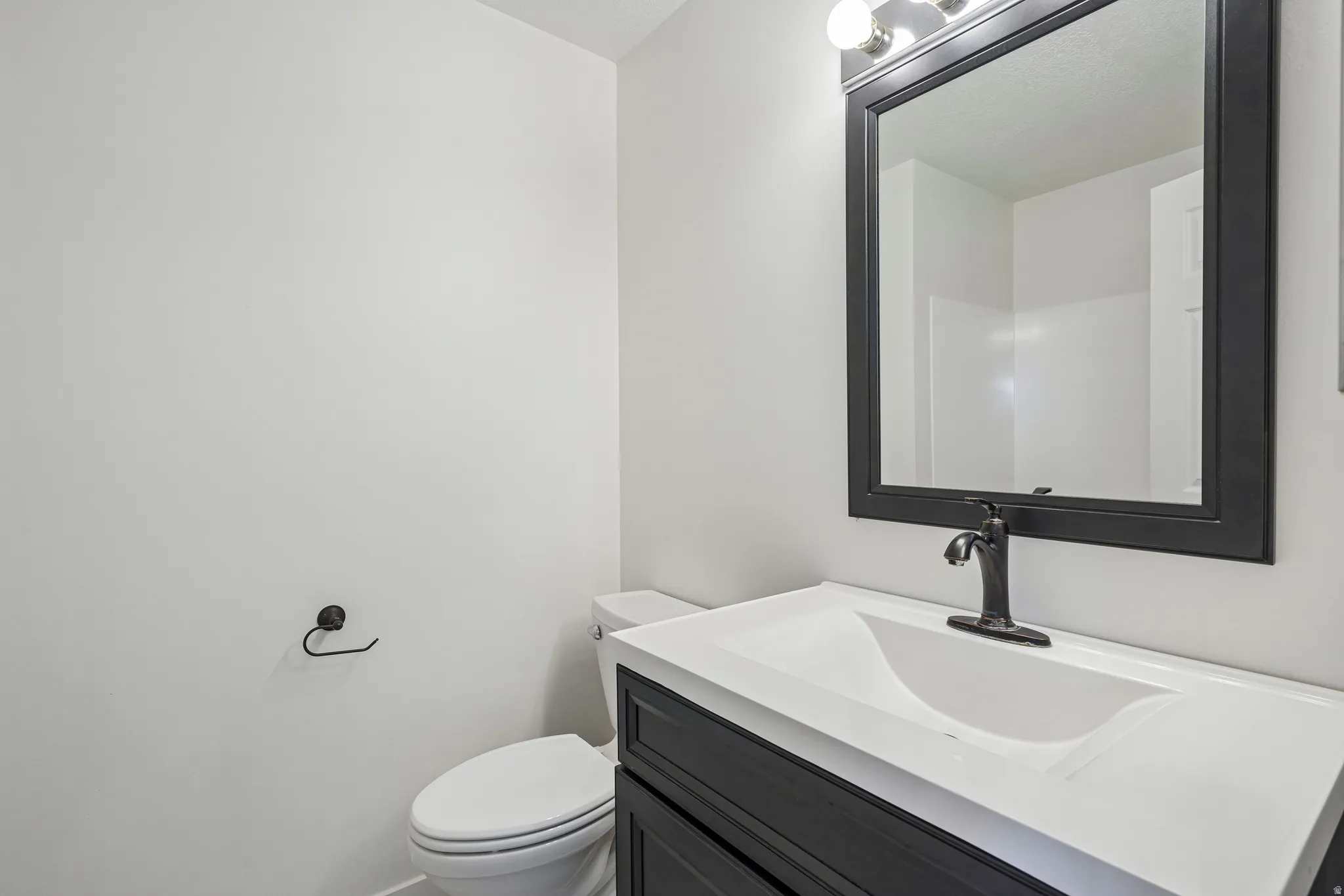 Bathroom featuring a black vanity with white countertop, black framed mirror, black faucet, and white toilet