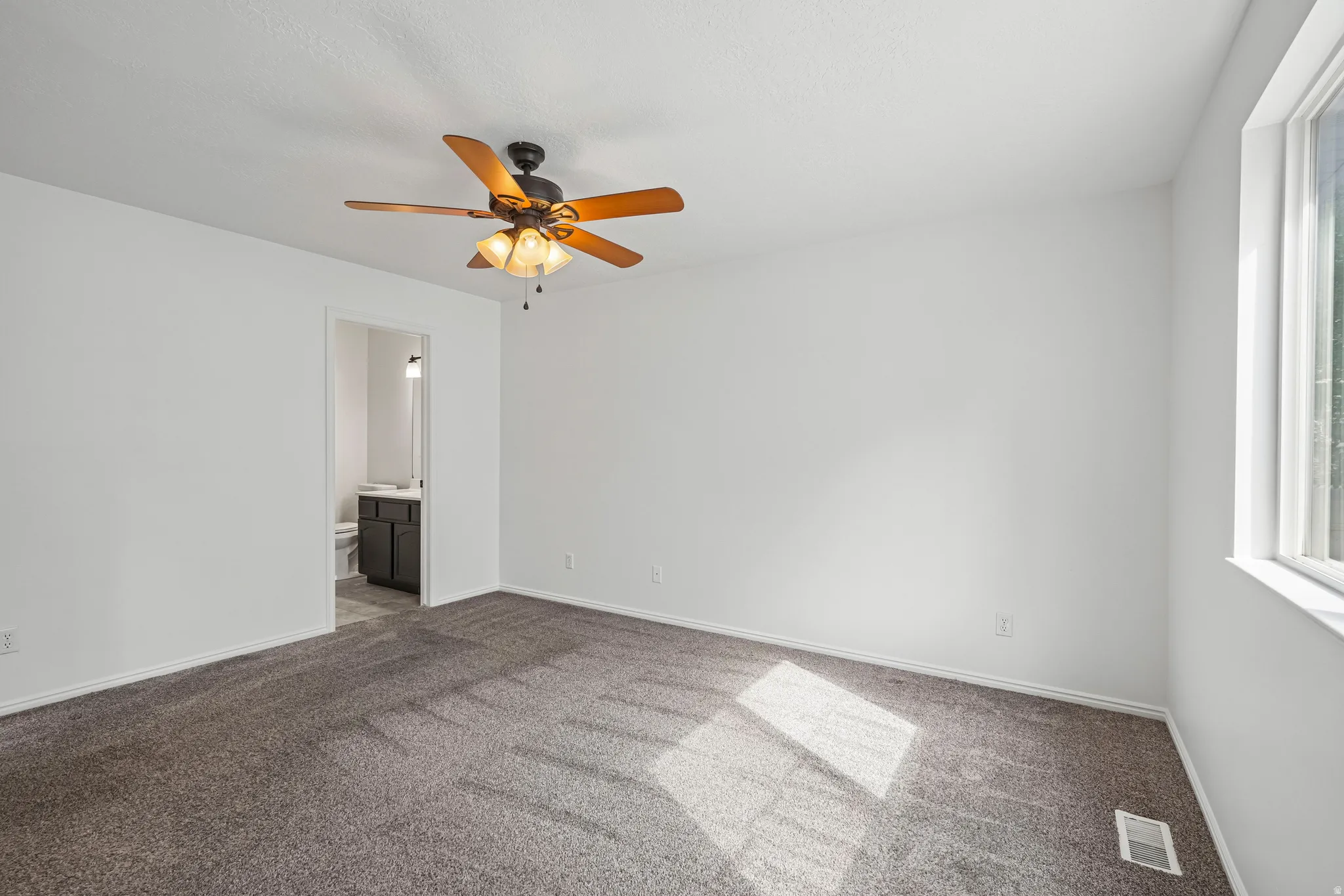 Spacious room featuring neutral carpeting, white walls, and a ceiling fan with light fixture