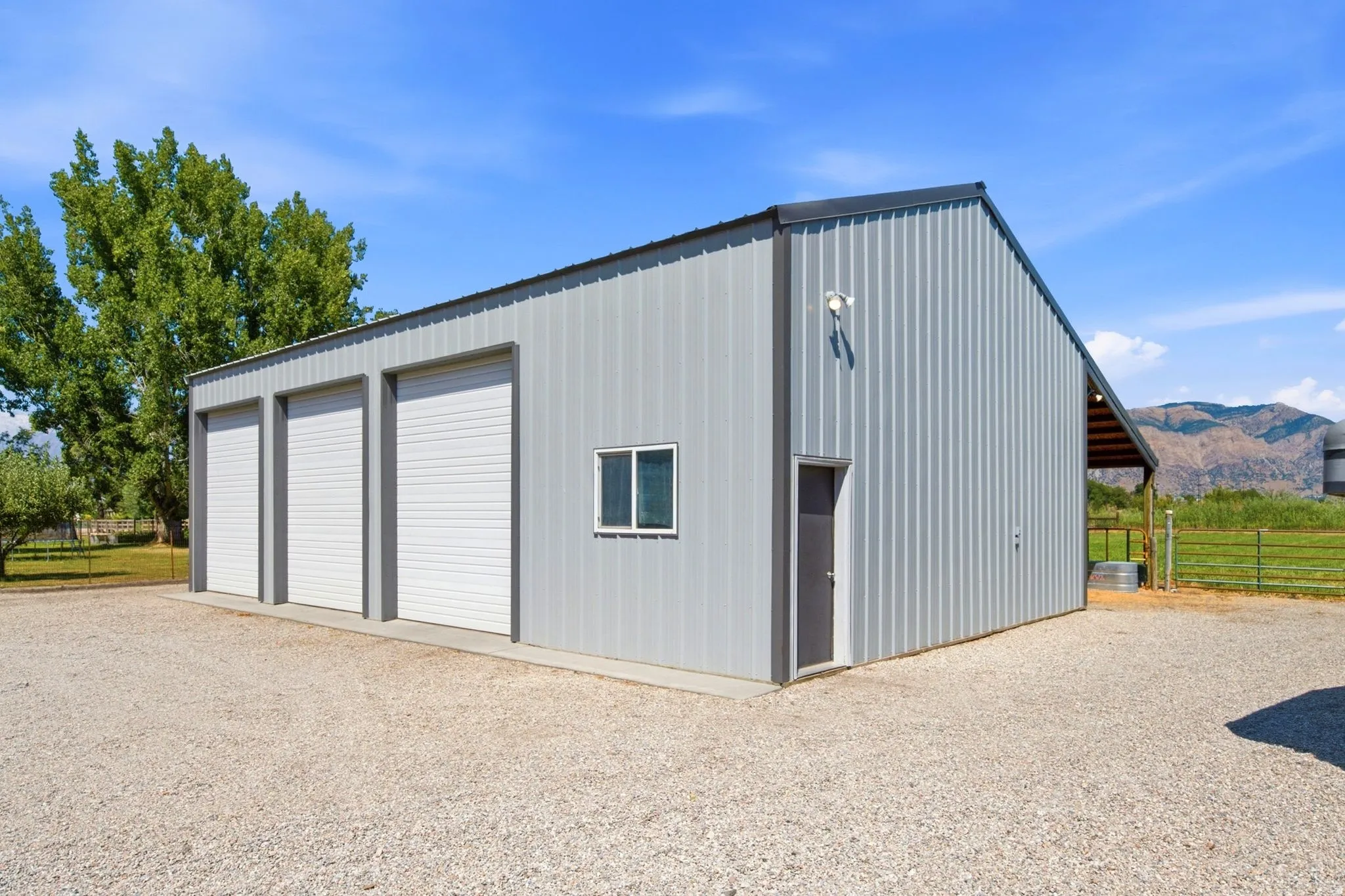 Galvanized metal outbuilding featuring three large roll-up doors, a side entry door, and a single window