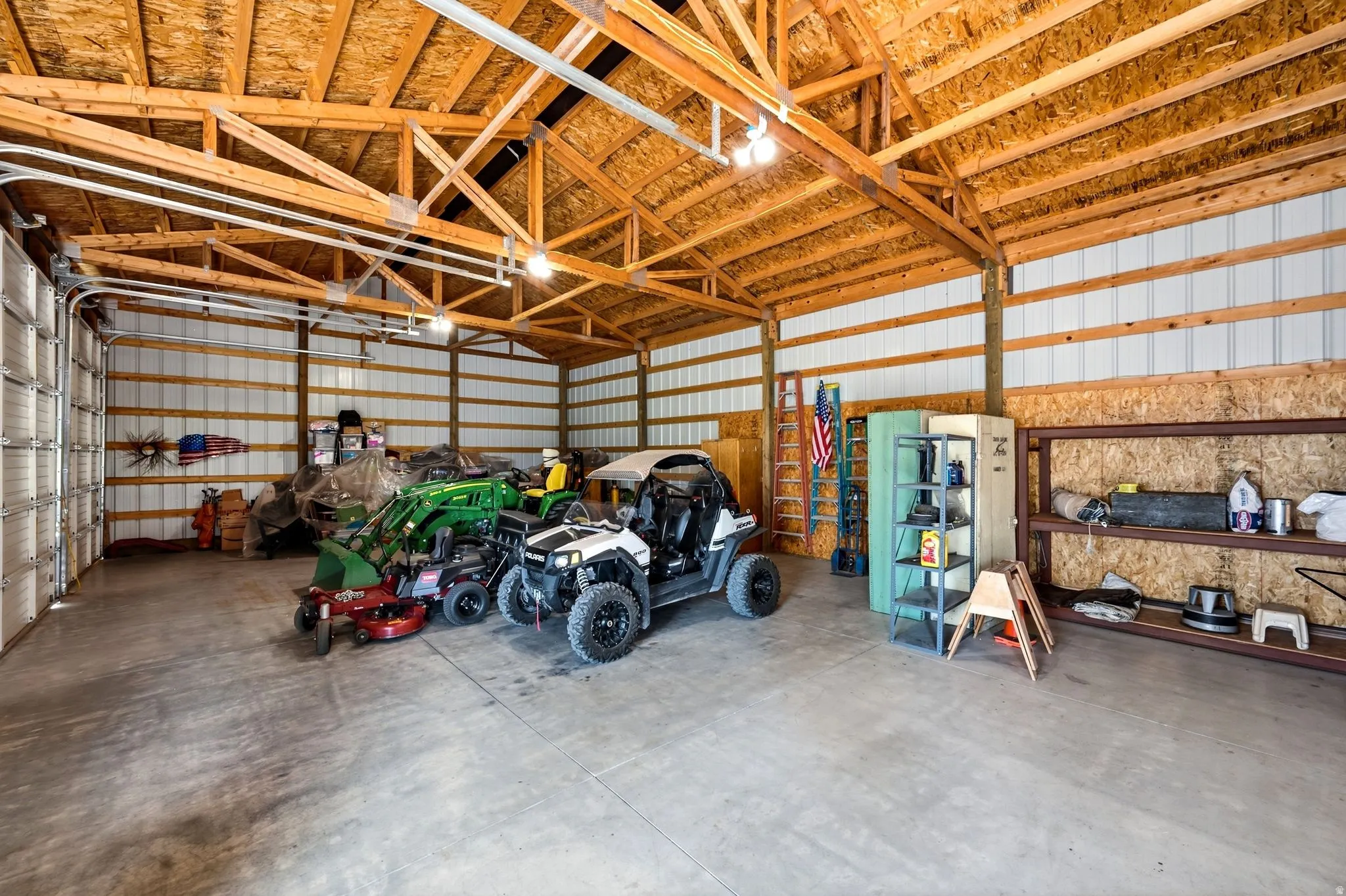 Spacious utility building featuring concrete flooring, exposed wood beam ceiling, metal-paneled walls, and two large roll-up doors for access