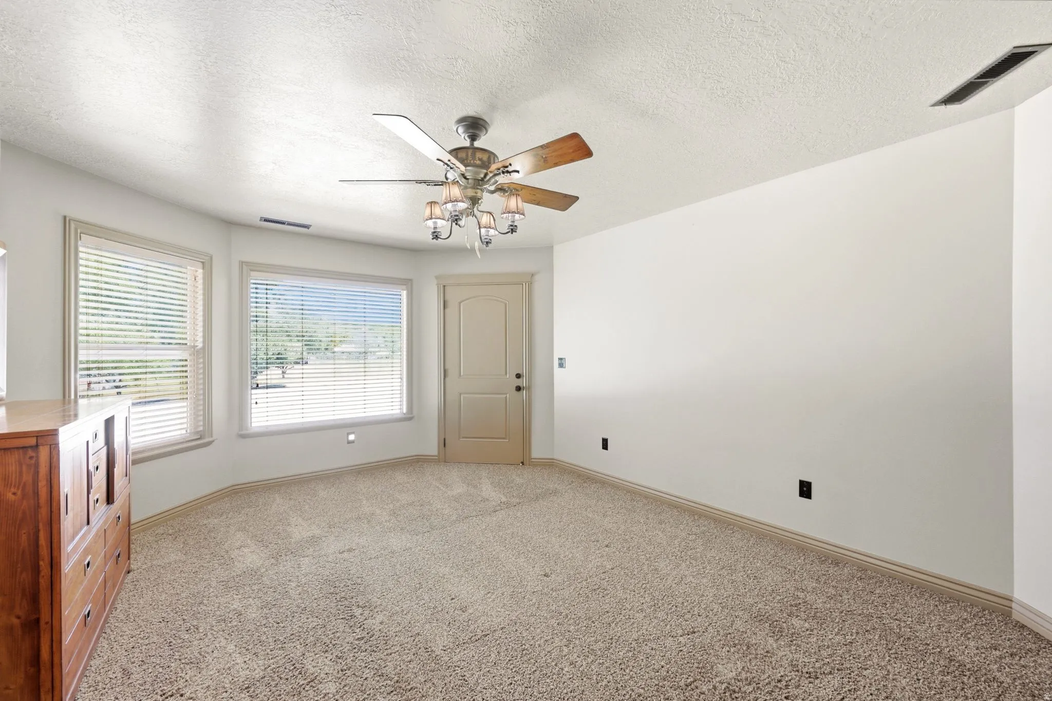 Carpeted interior space featuring multiple large windows with horizontal blinds, a ceiling fan with integrated lighting, and a neutral wall palette