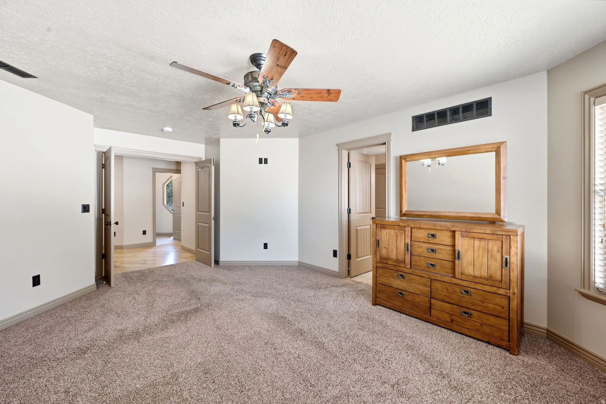 Spacious room featuring neutral carpeting, a ceiling fan with integrated lighting, and multiple doorways providing access to other areas