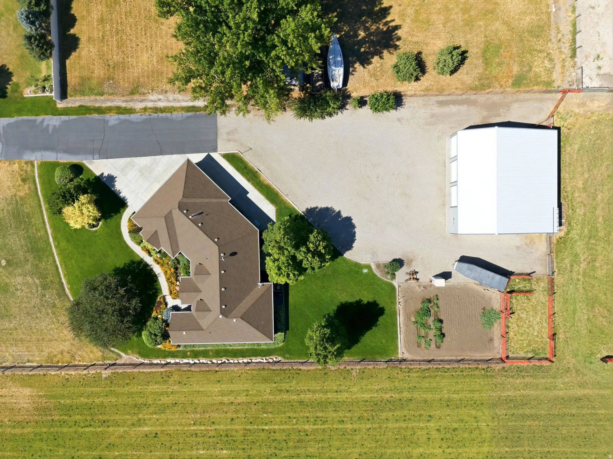 Expansive property featuring a residence with a multi-gabled roofline, a large paved driveway, a separate outbuilding with multiple bay doors, and a cultivated garden area