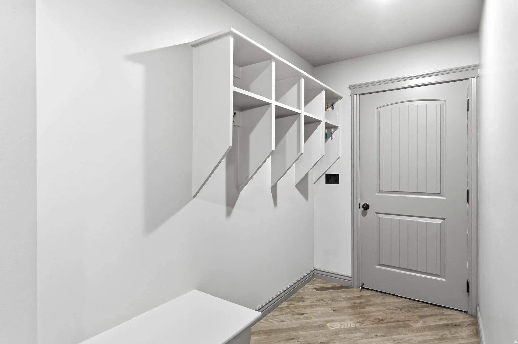 Entryway featuring built-in white cubby storage with hooks, a built-in bench, a paneled interior door with black hardware, and wood-finish flooring