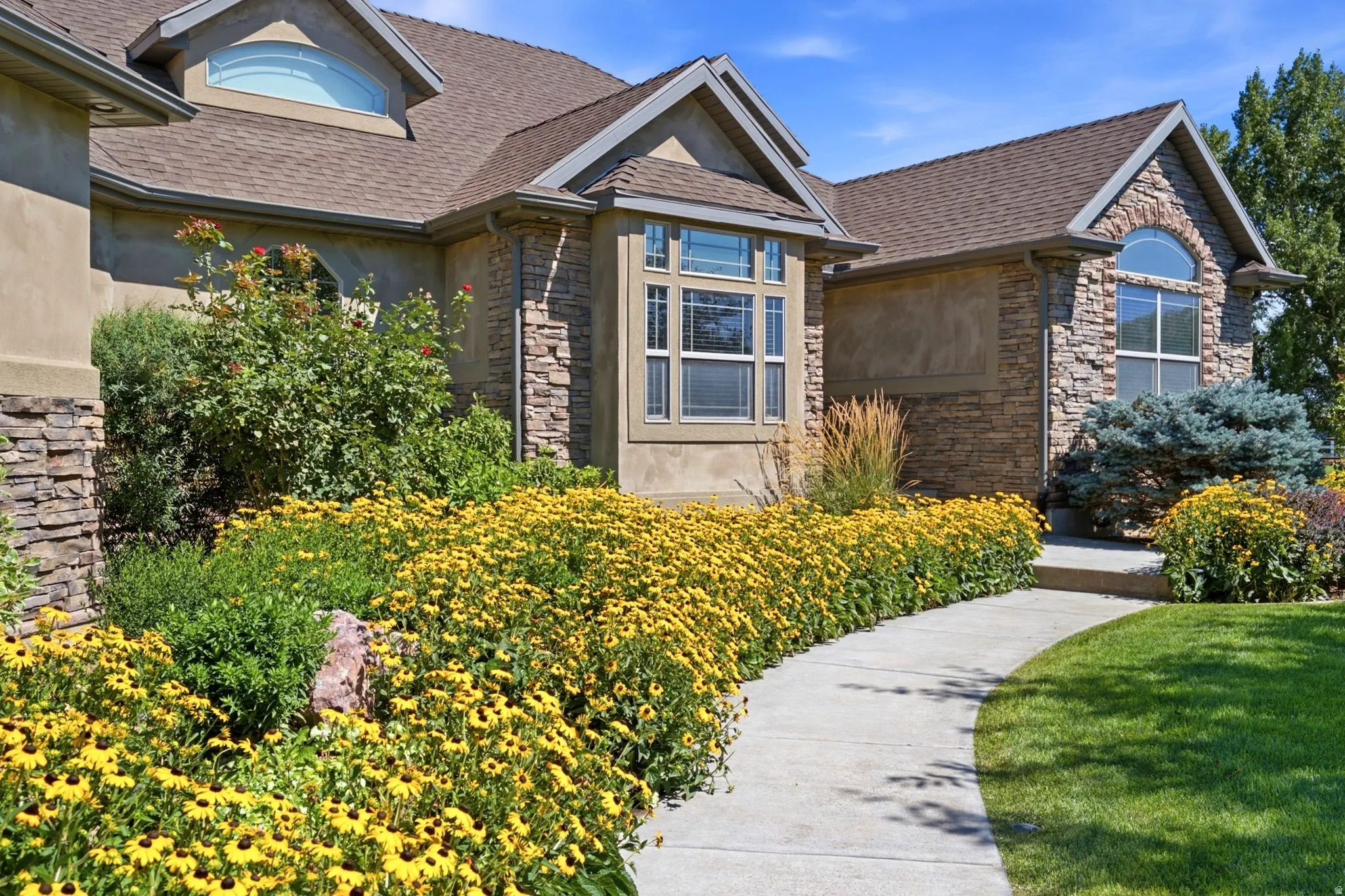 Stone and stucco exterior featuring a curved walkway, established landscaping, arched transom windows, and a bay window
