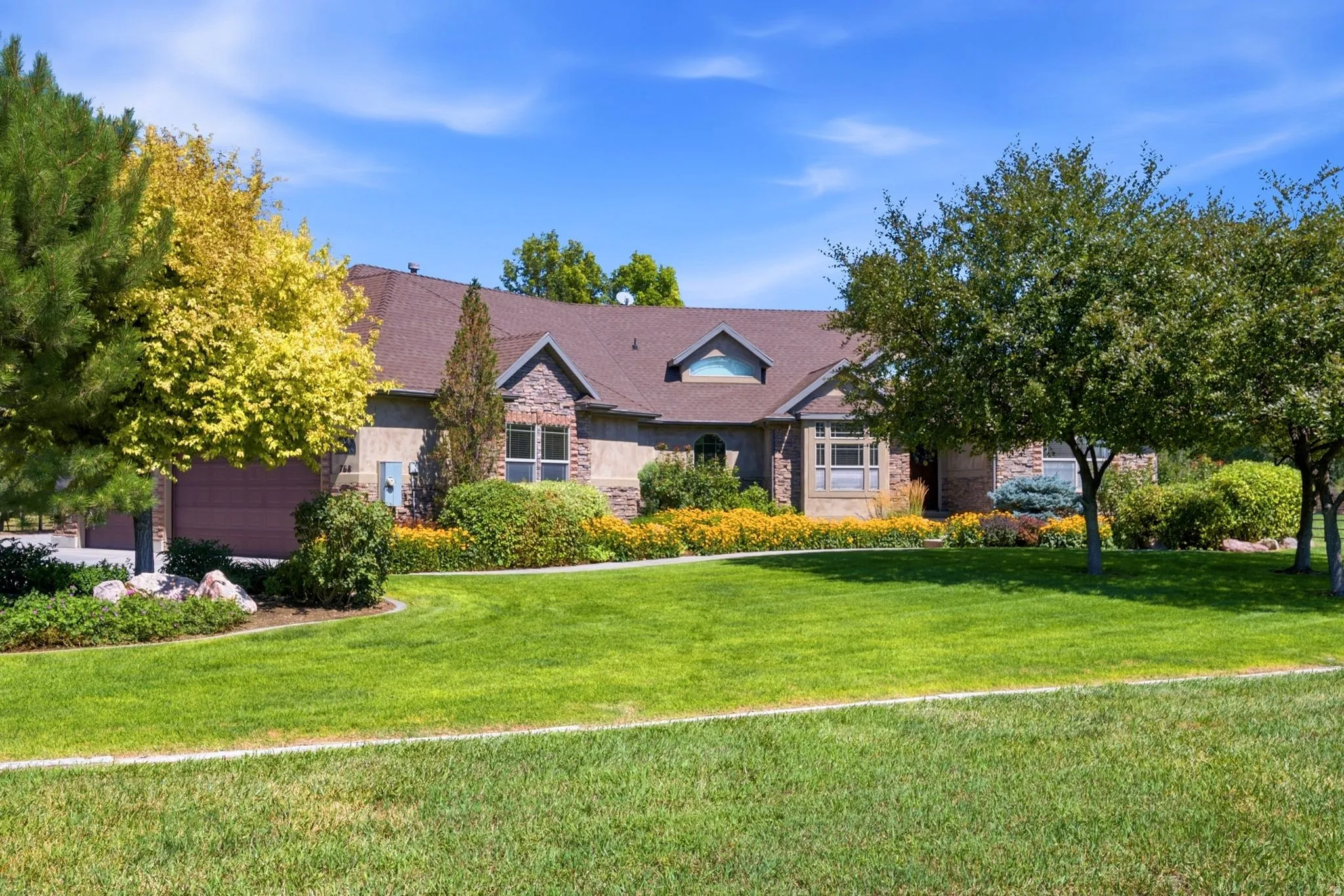 Stone and stucco exterior featuring a multi-gabled roofline, dual garage doors, and mature landscaping