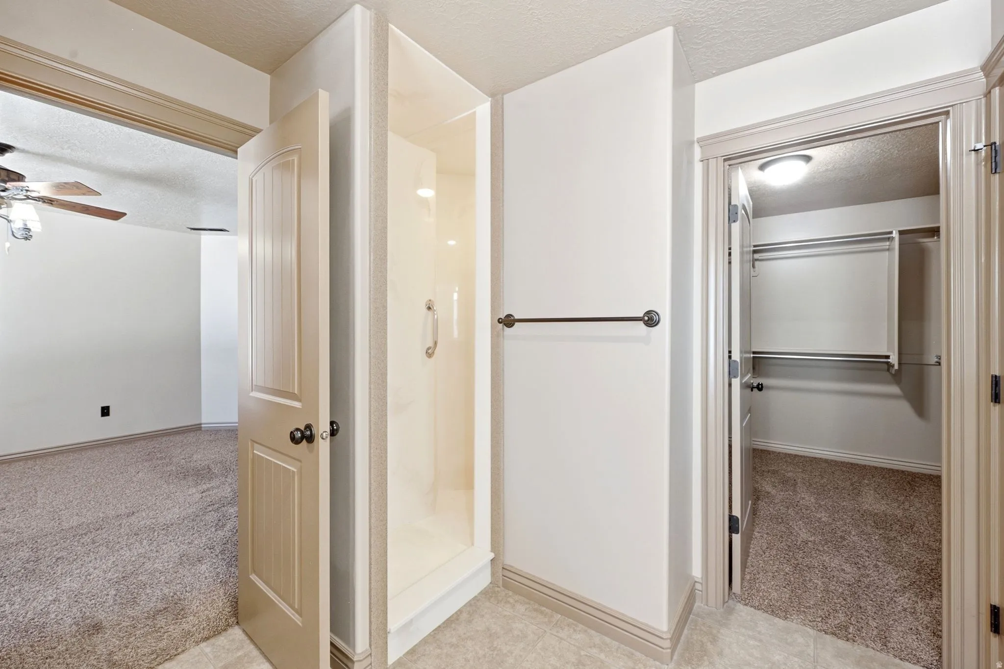 Walk-in shower with clear enclosure, towel bar, and adjacent closet with built-in shelving and hanging rods