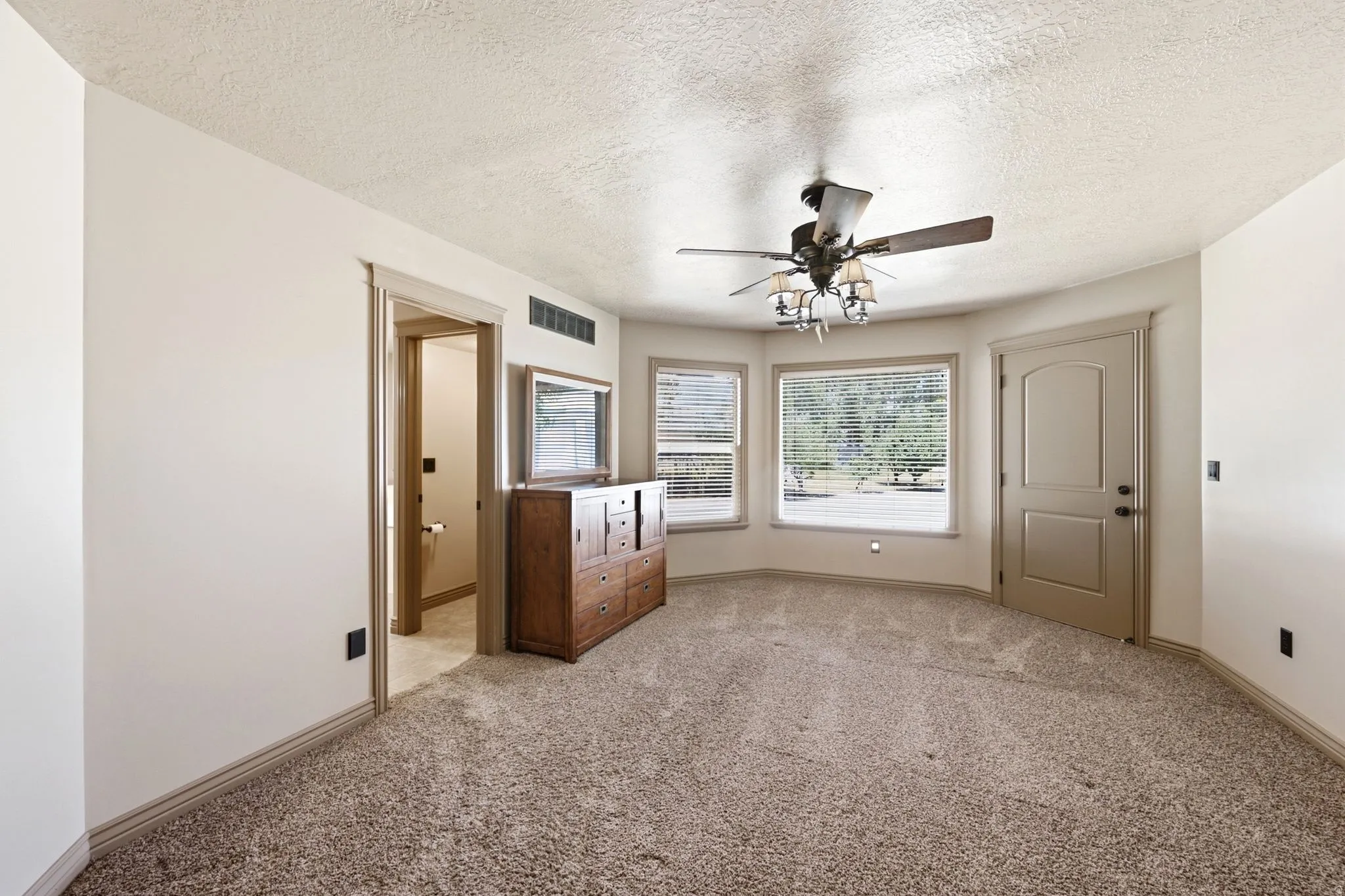 Carpeted interior space featuring a ceiling fan with integrated lighting, a bay window with multiple panes, a recessed door, and a doorway opening to an additional room