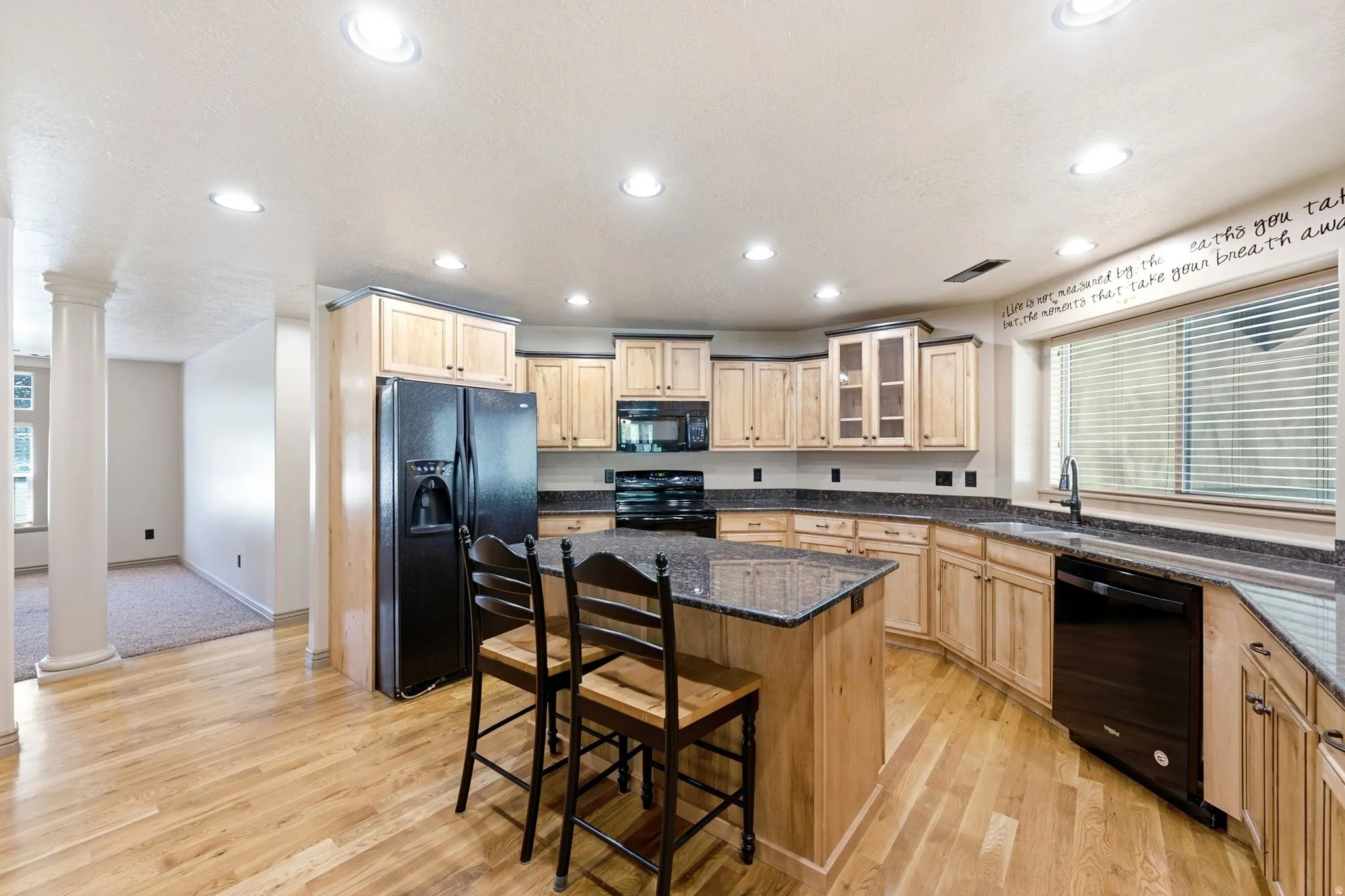 Spacious kitchen featuring a central island with countertop seating, light wood-finish cabinetry, dark stone countertops, and recessed lighting