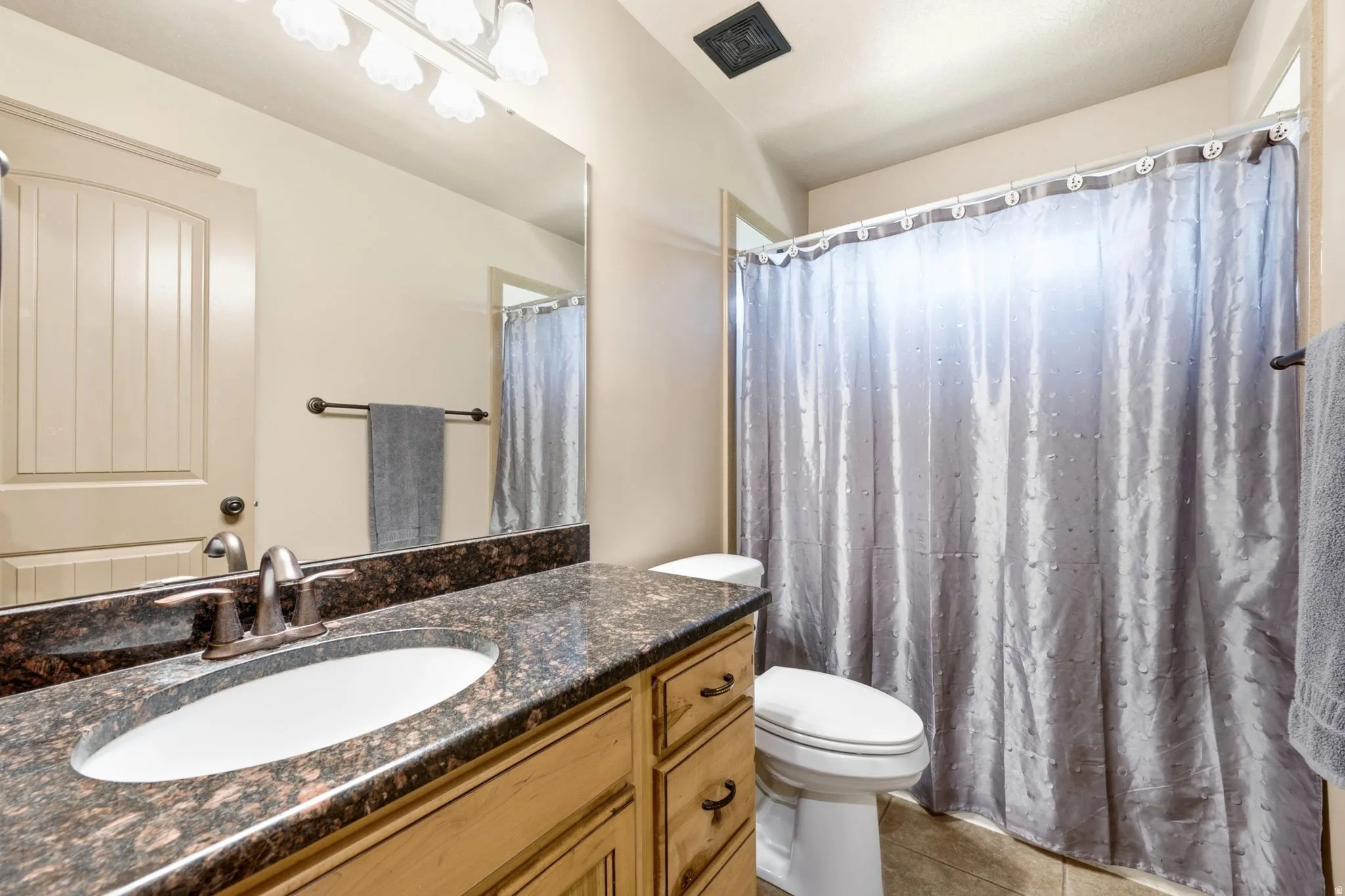 Bathroom featuring a single vanity with a dark speckled countertop, an oval undermount sink, and wood-finish cabinetry