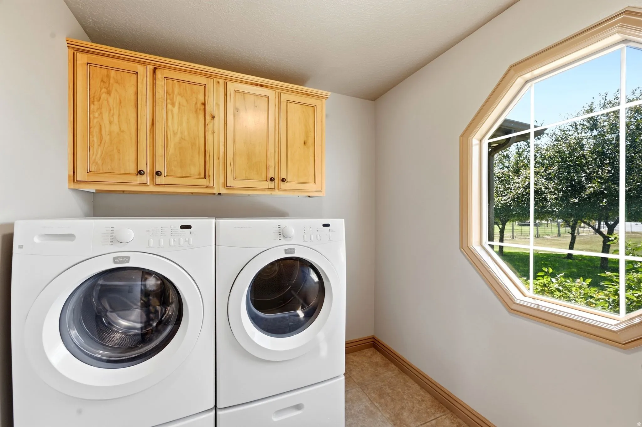 Laundry area featuring natural wood cabinetry, an octagonal window, and tiled flooring