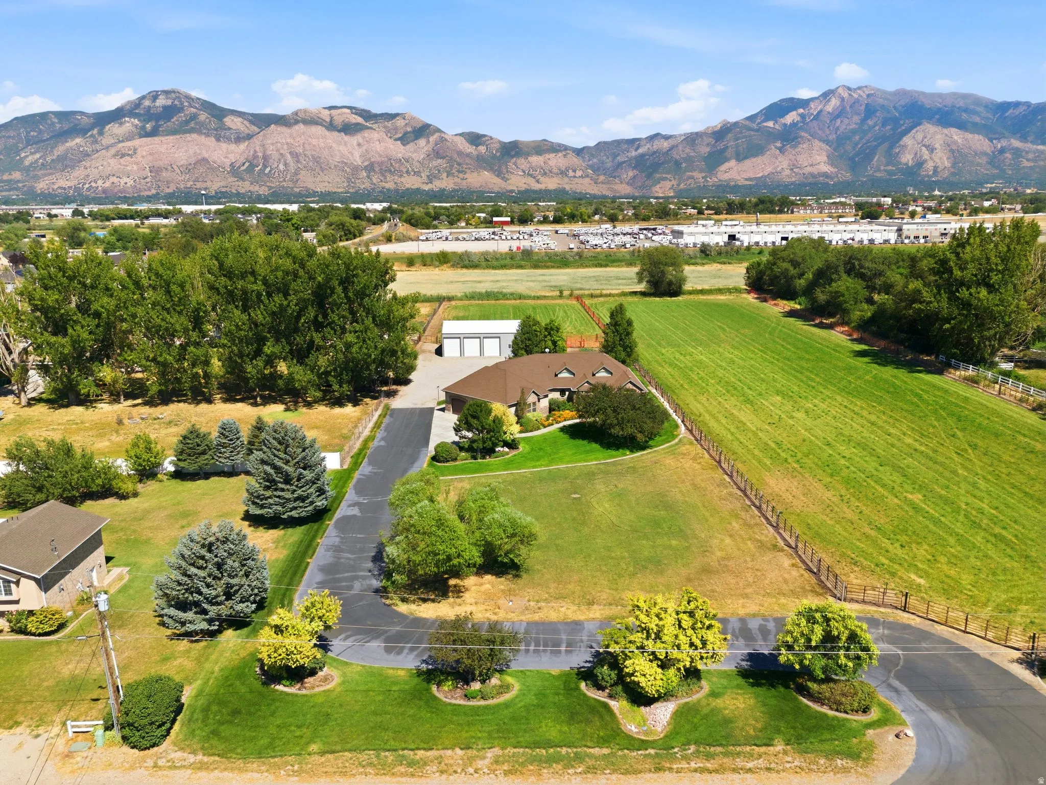 Expansive property featuring a single-story residence with a brown shingle roof, a paved driveway, and detached garages