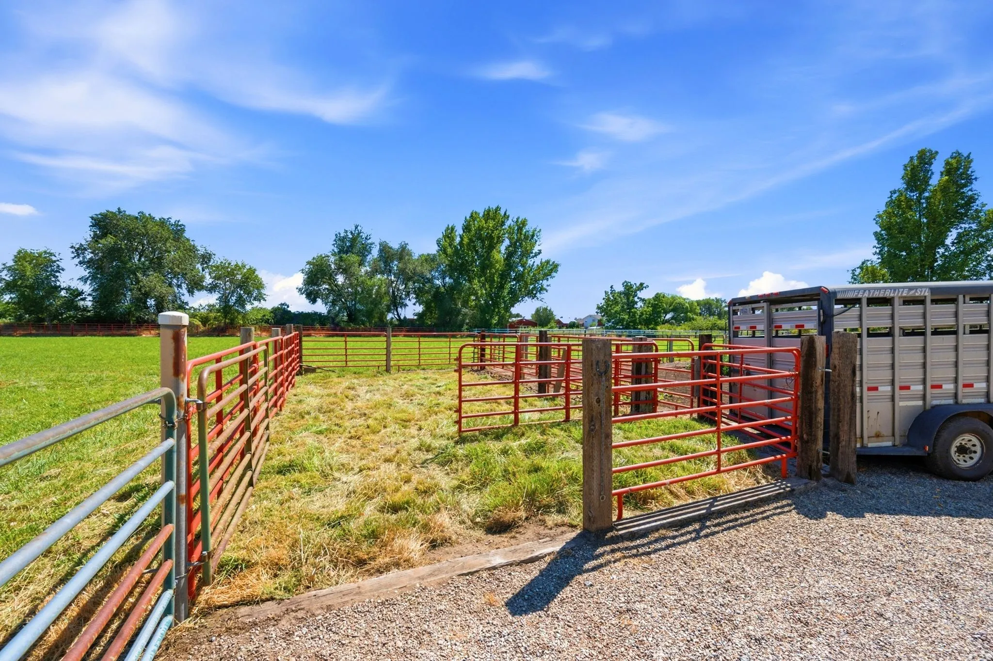 Fenced outdoor enclosure featuring red metal gates, wooden posts, and a gravel surface