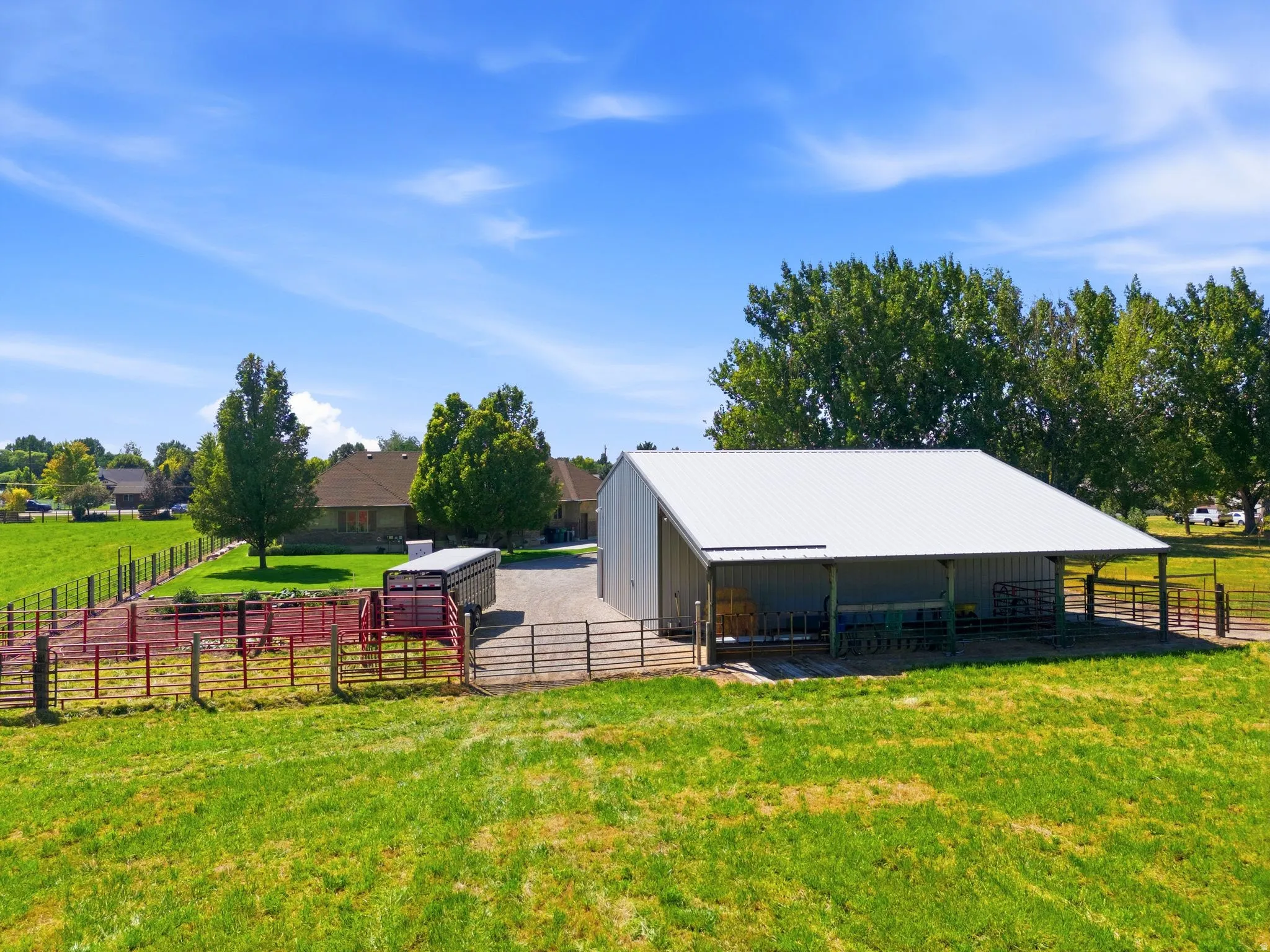 Metal barn structure featuring a covered lean-to, multiple fenced enclosures, and gravel drive
