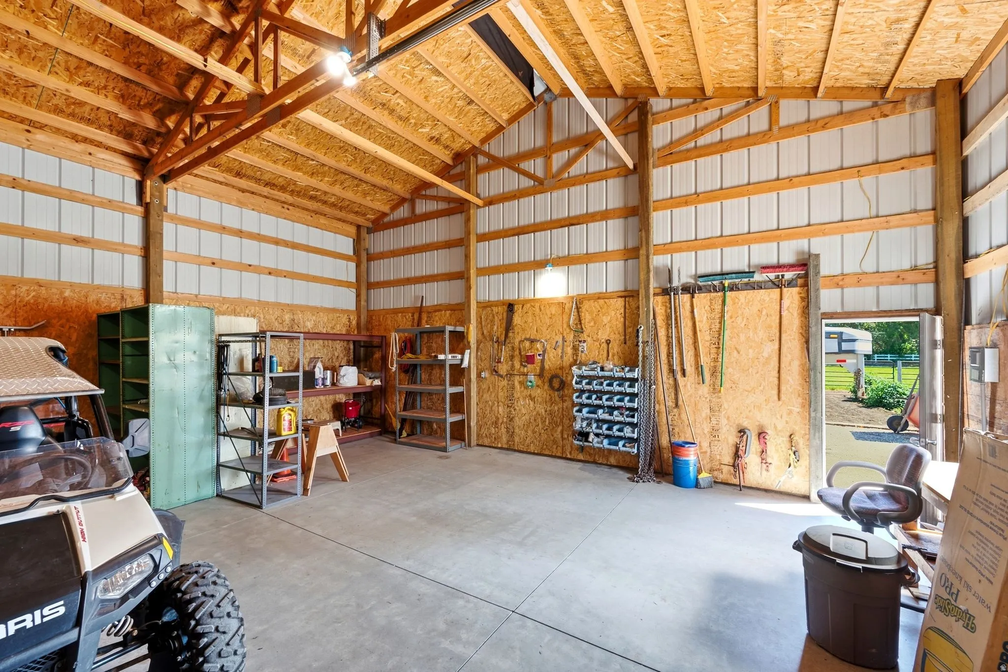 Spacious garage or workshop featuring a concrete floor, exposed wood beam ceiling, metal siding walls, and a dedicated entry door