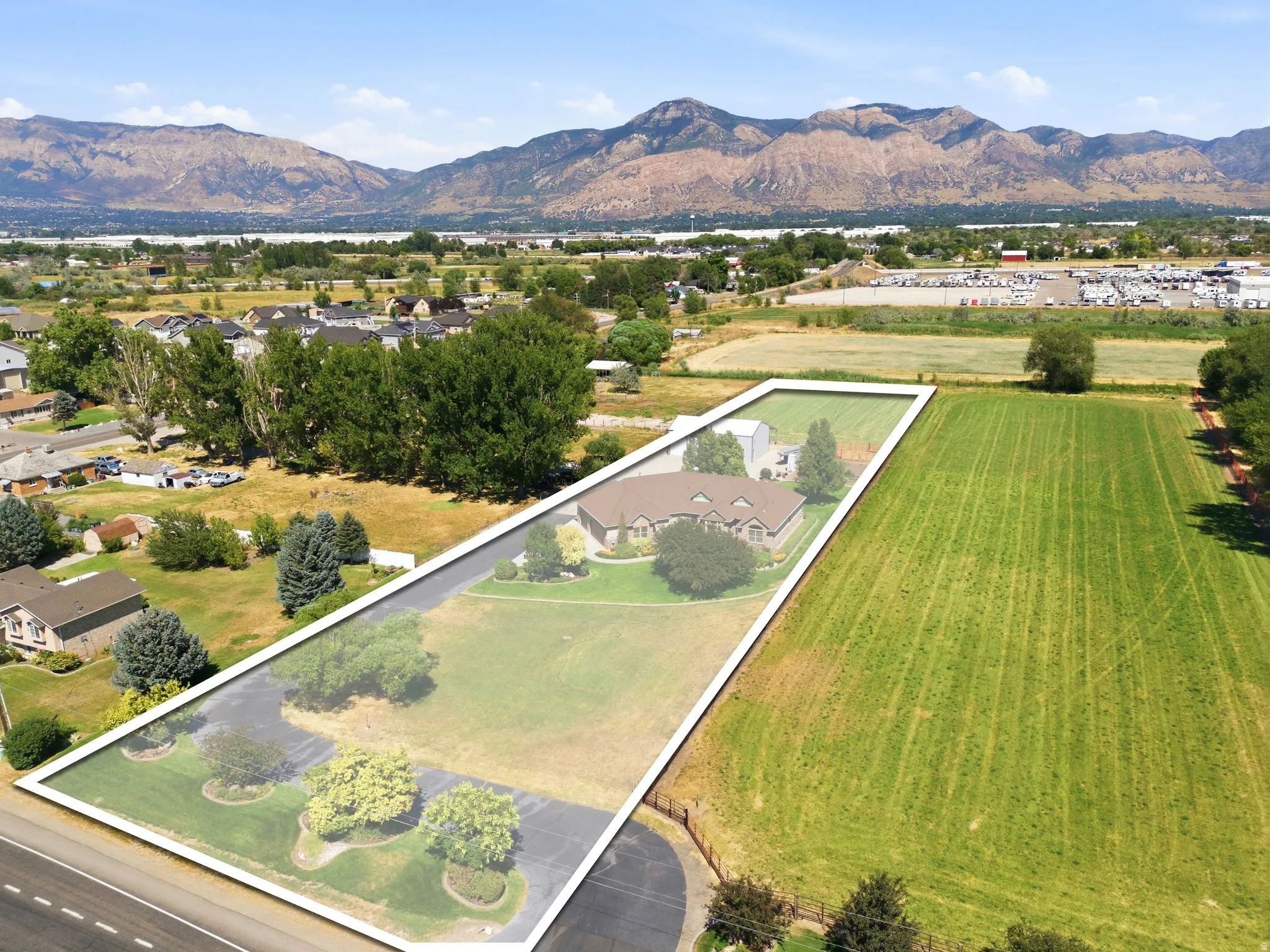 Expansive property featuring a single-story residence, mature landscaping, paved driveway, and a large grassy field