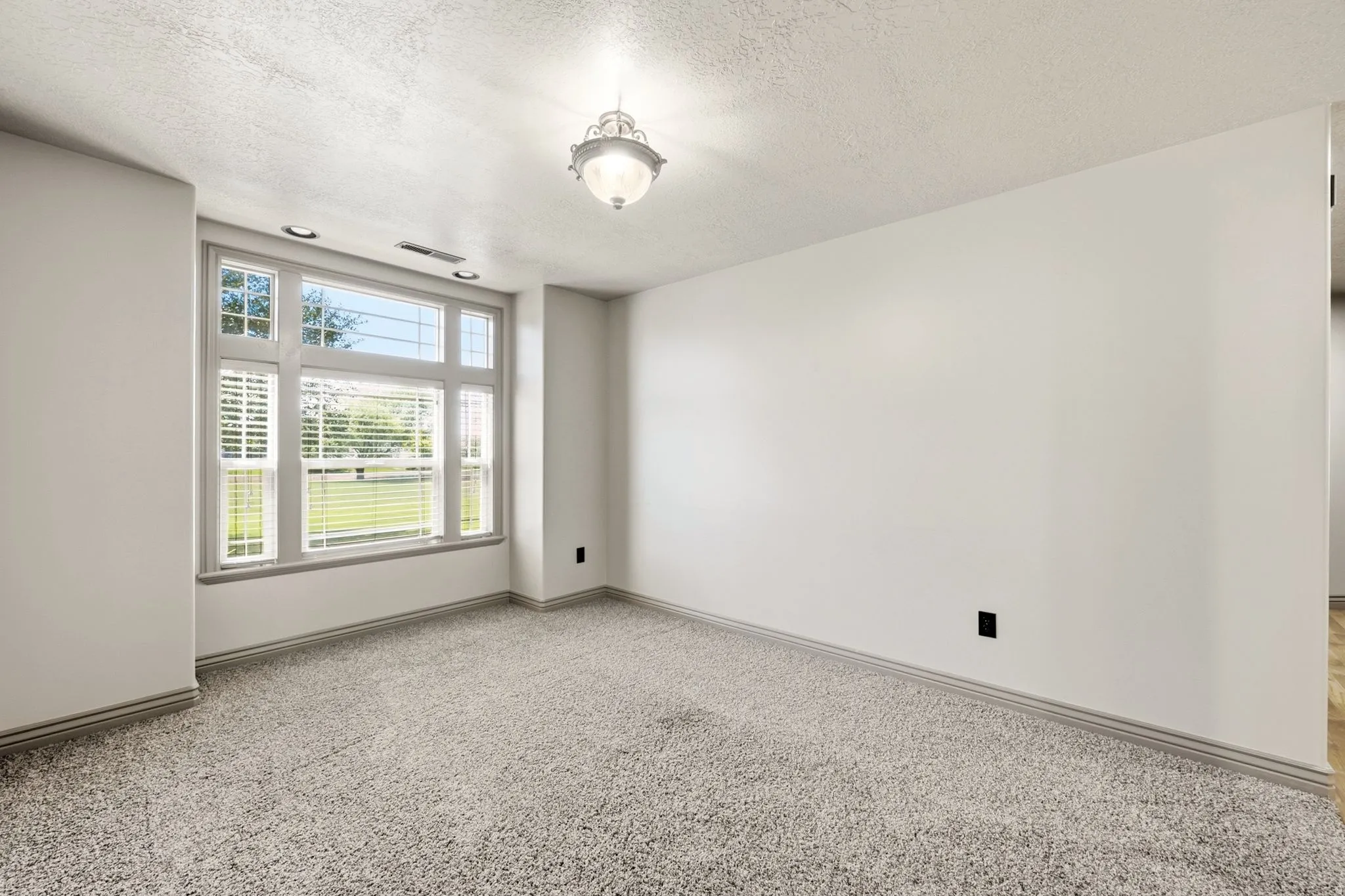 Spacious room featuring a large multi-pane window with blinds, recessed lighting, a central semi-flush mount fixture, and light-colored carpet flooring